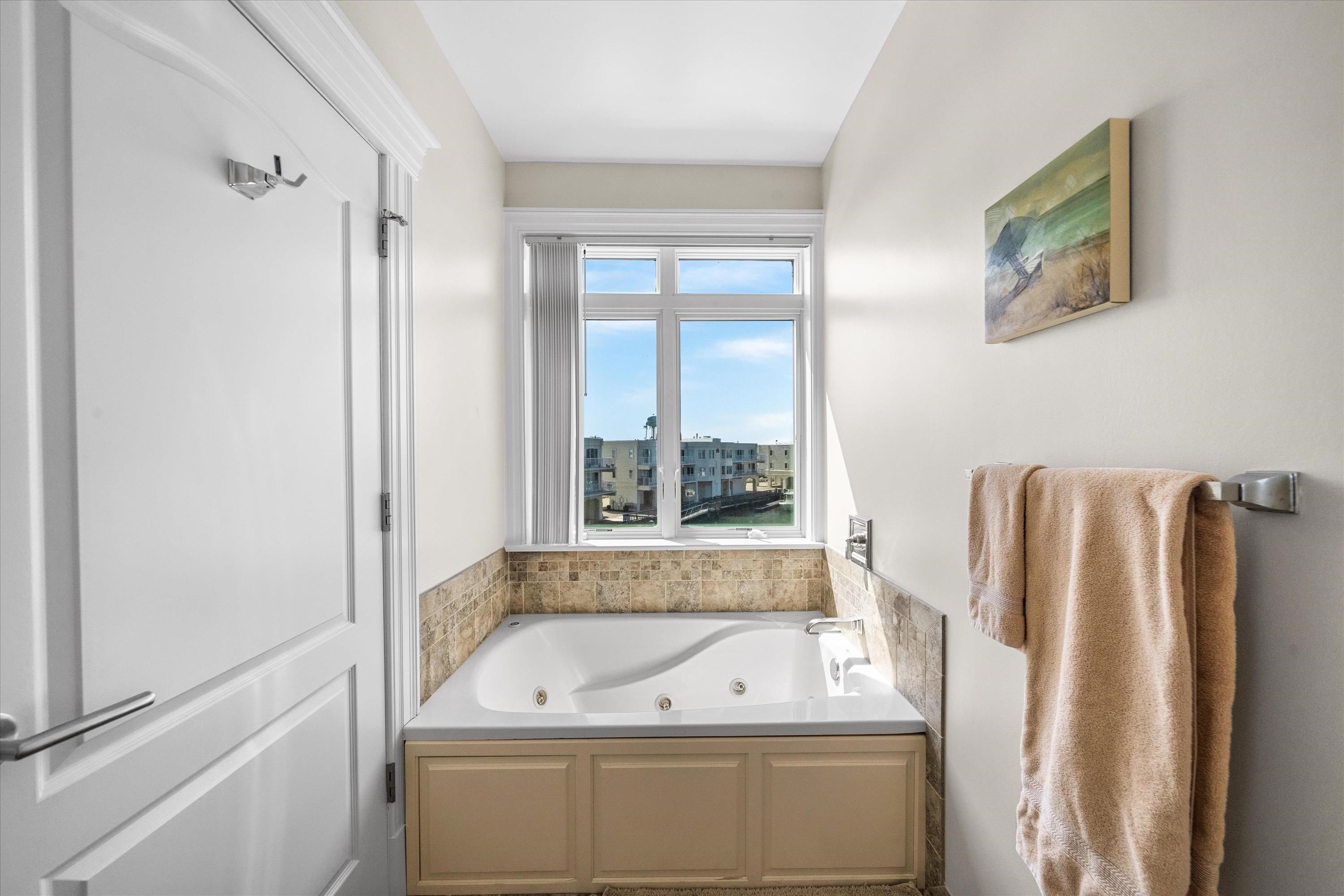 Bathroom with a jetted tub beneath a large window overlooking nearby buildings.