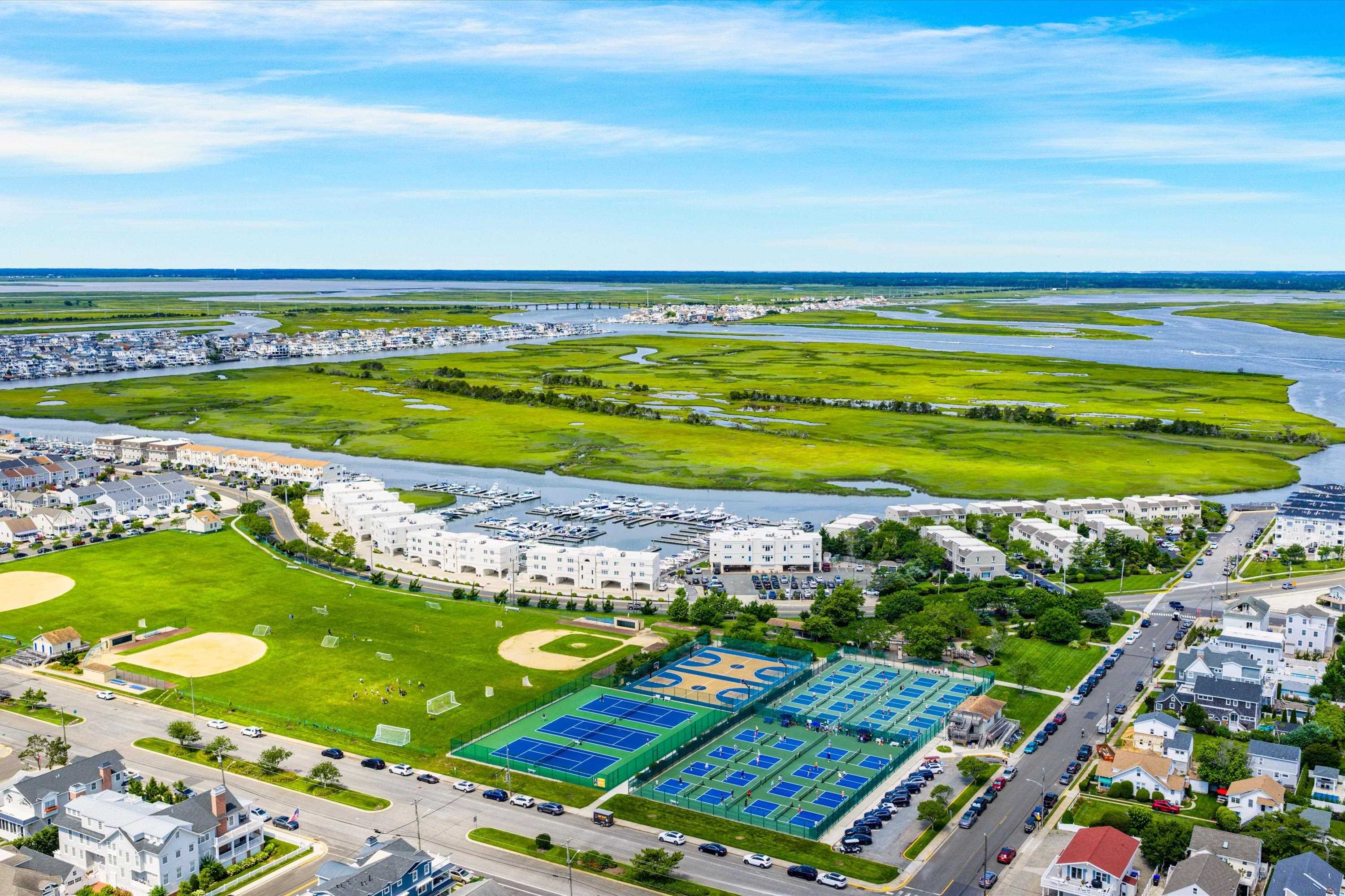 Aerial view of a waterfront community with a marina, tennis courts, sports fields, and surrounding marshland.