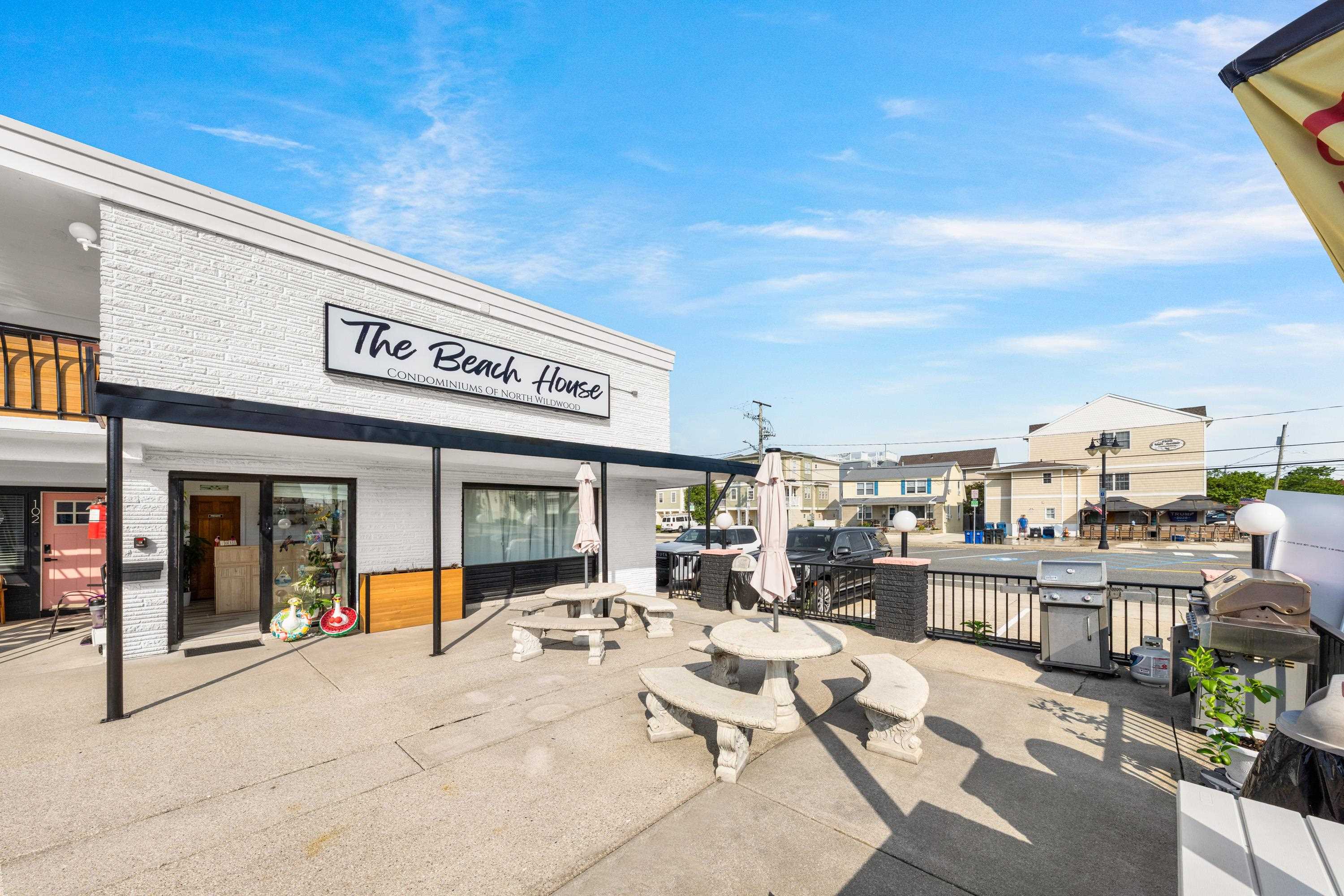 Beach House condominium exterior with a sunny patio, stone picnic tables, umbrellas, and grills.