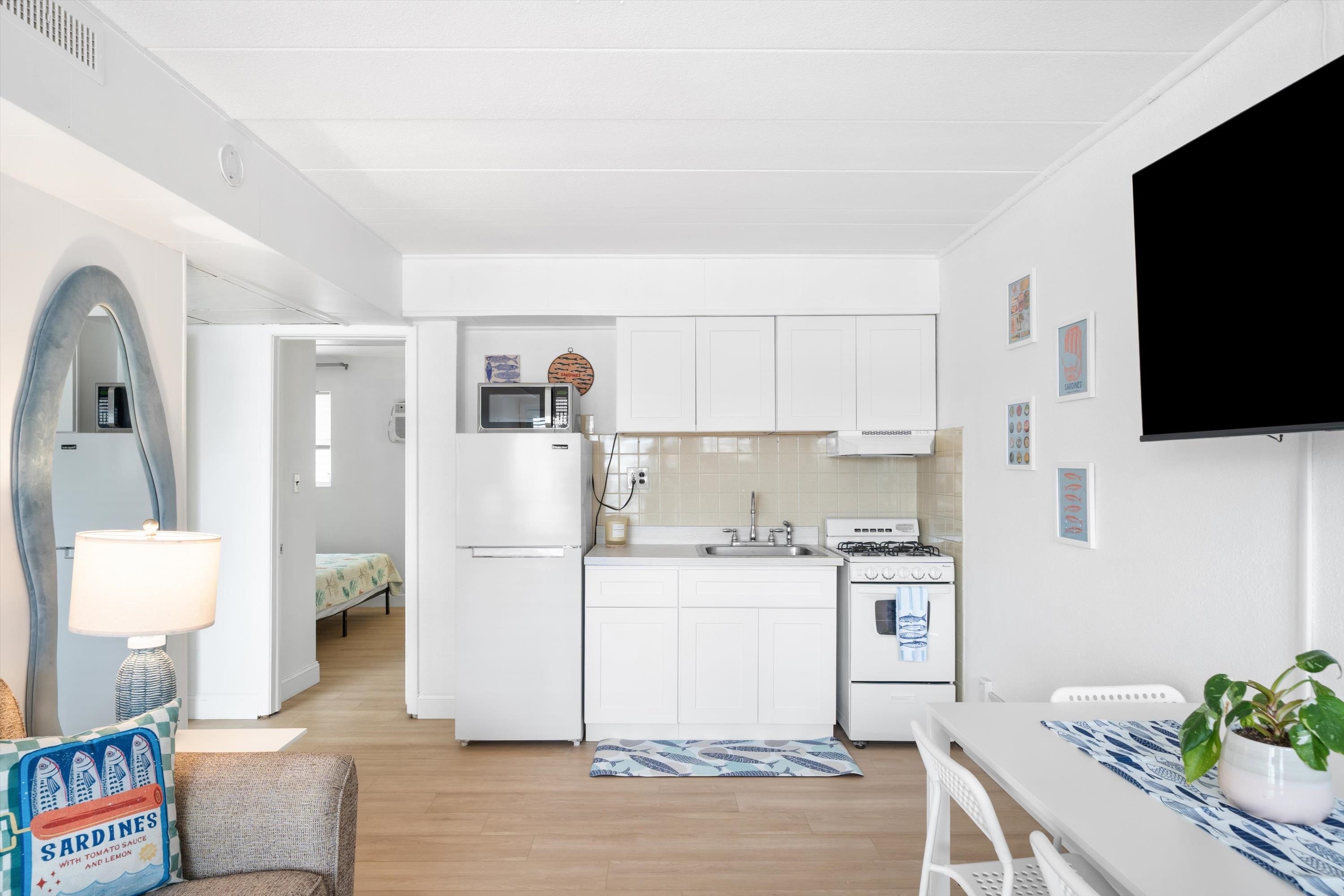 Compact white kitchenette with a microwave and gas stove, opening onto a bedroom.