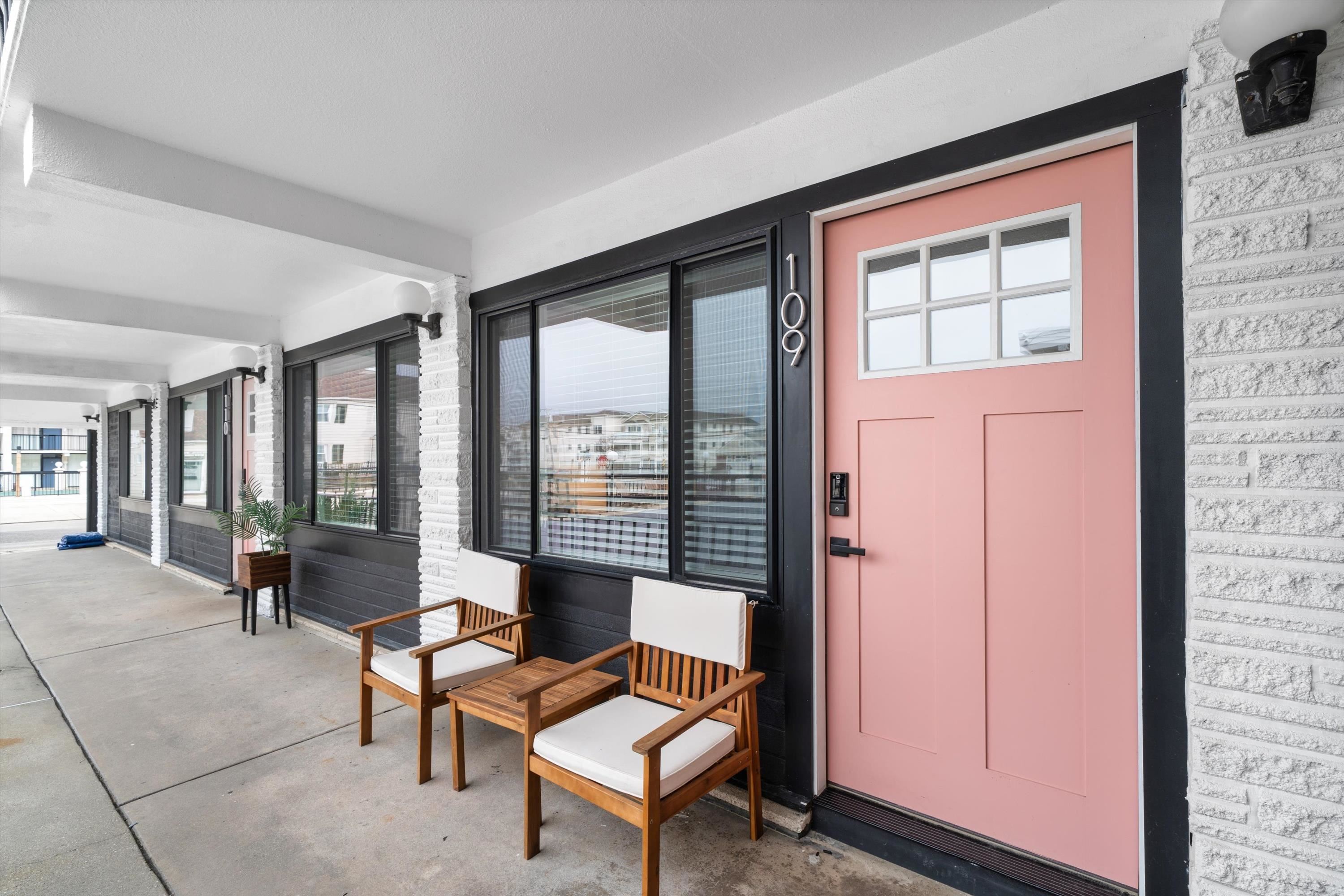 Condominium entrance with a pink door marked 109 and two chairs along a covered walkway.