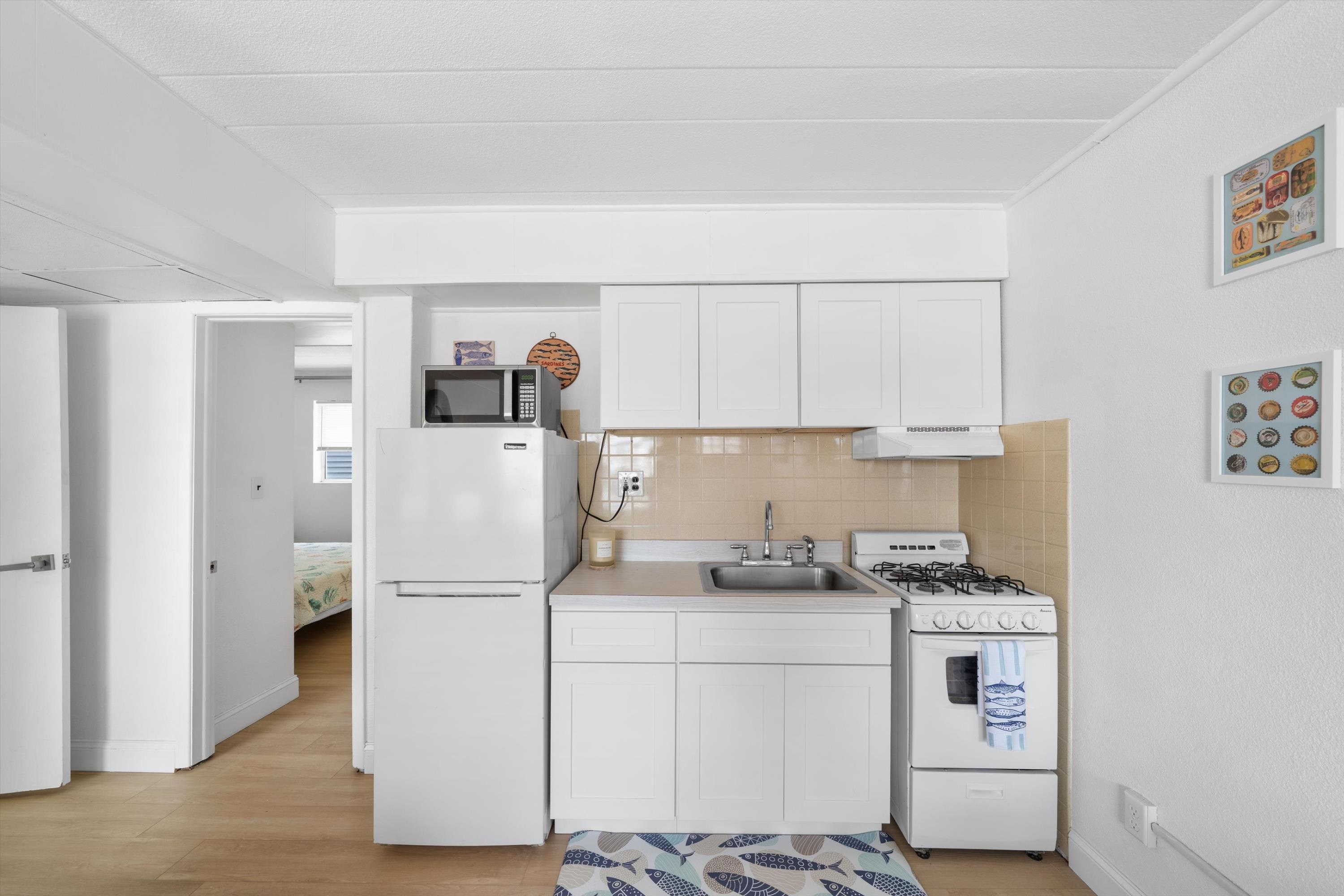Compact condo kitchen with white cabinets, beige tile backsplash, refrigerator, sink, and gas range.