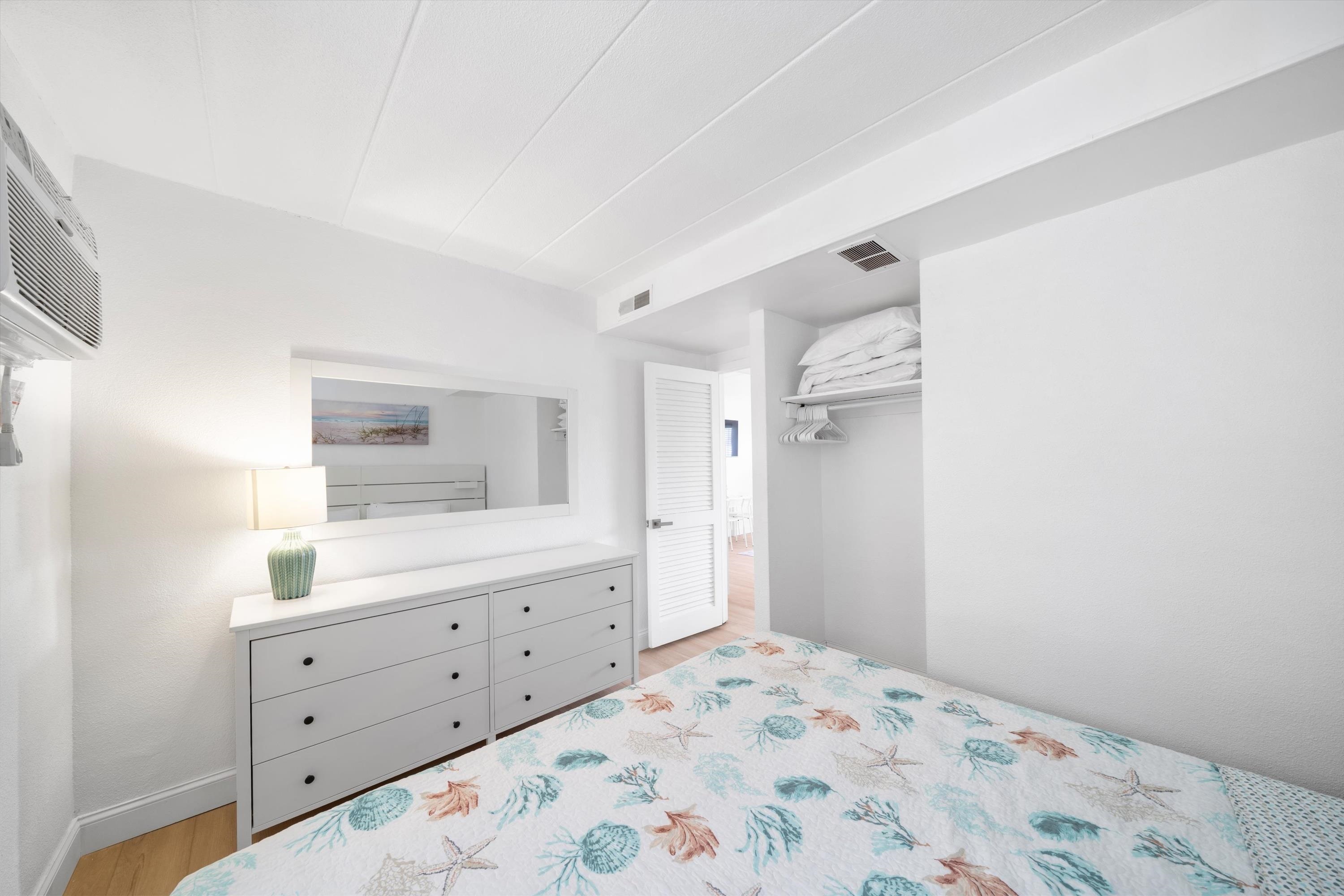 Bedroom with a seashell-patterned bedspread, white dresser, wall mirror, and open closet.