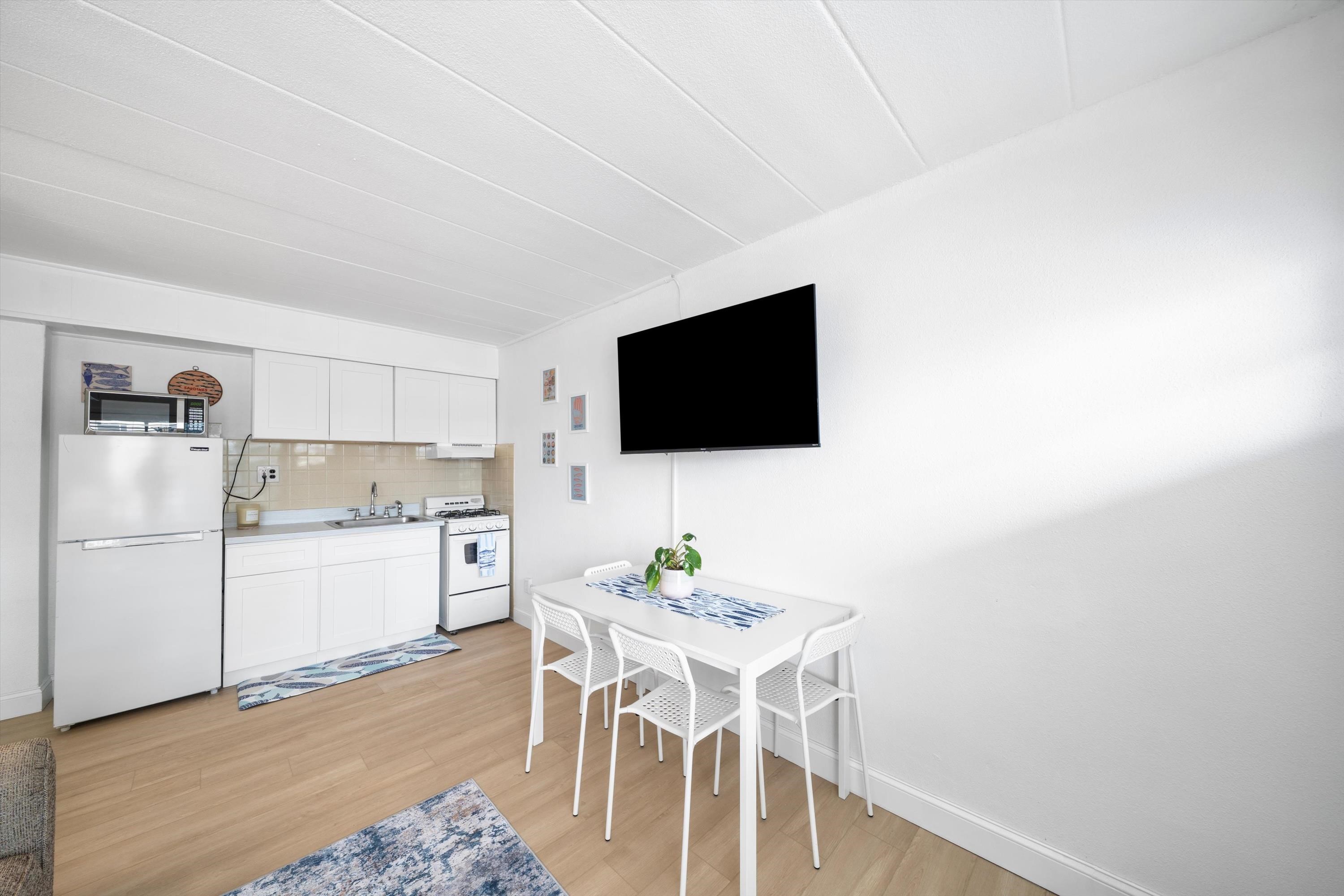 Compact white kitchen and dining area with a table, chairs, and wall-mounted television.