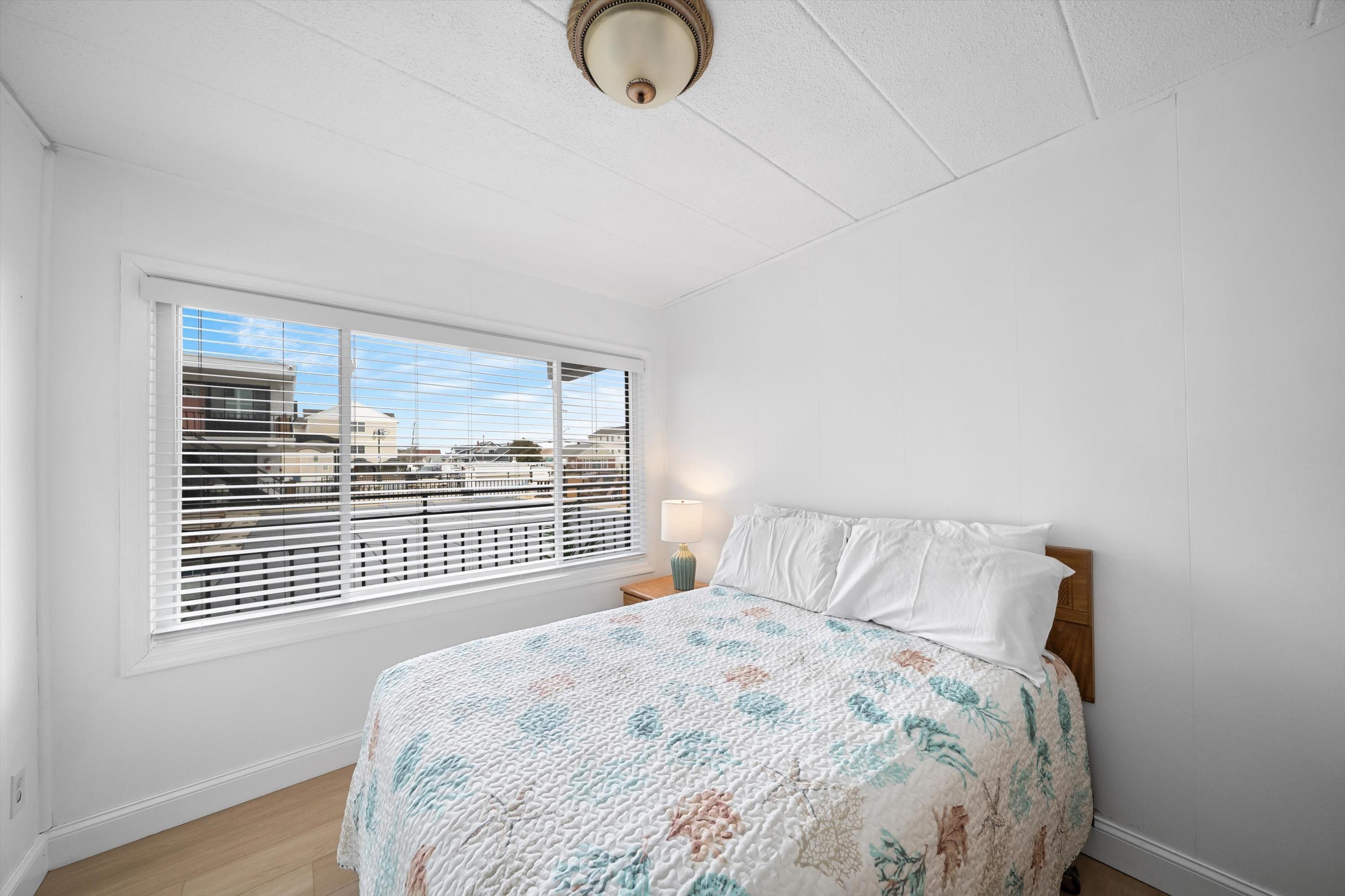 Bedroom with a patterned quilt-covered bed beside a wide window with blinds.