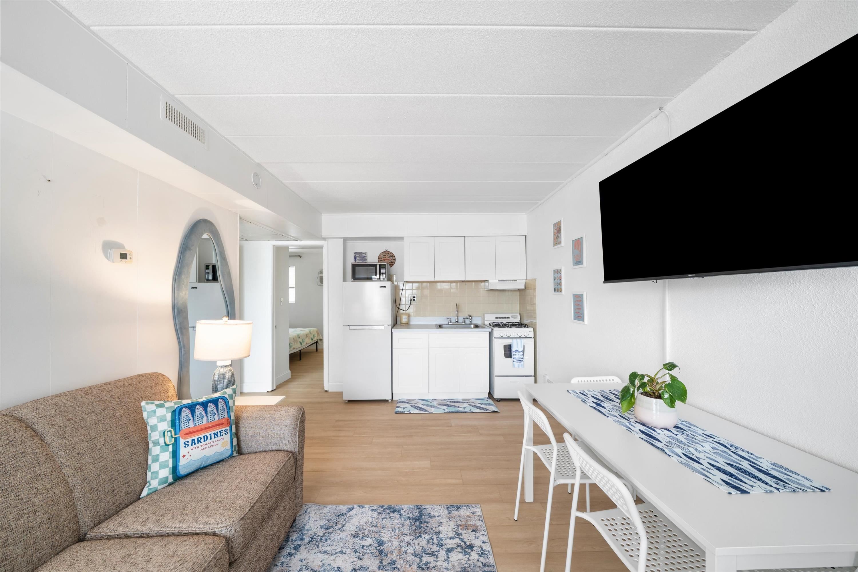Furnished living and dining area with a compact kitchen, brown sofa, and white dining table.