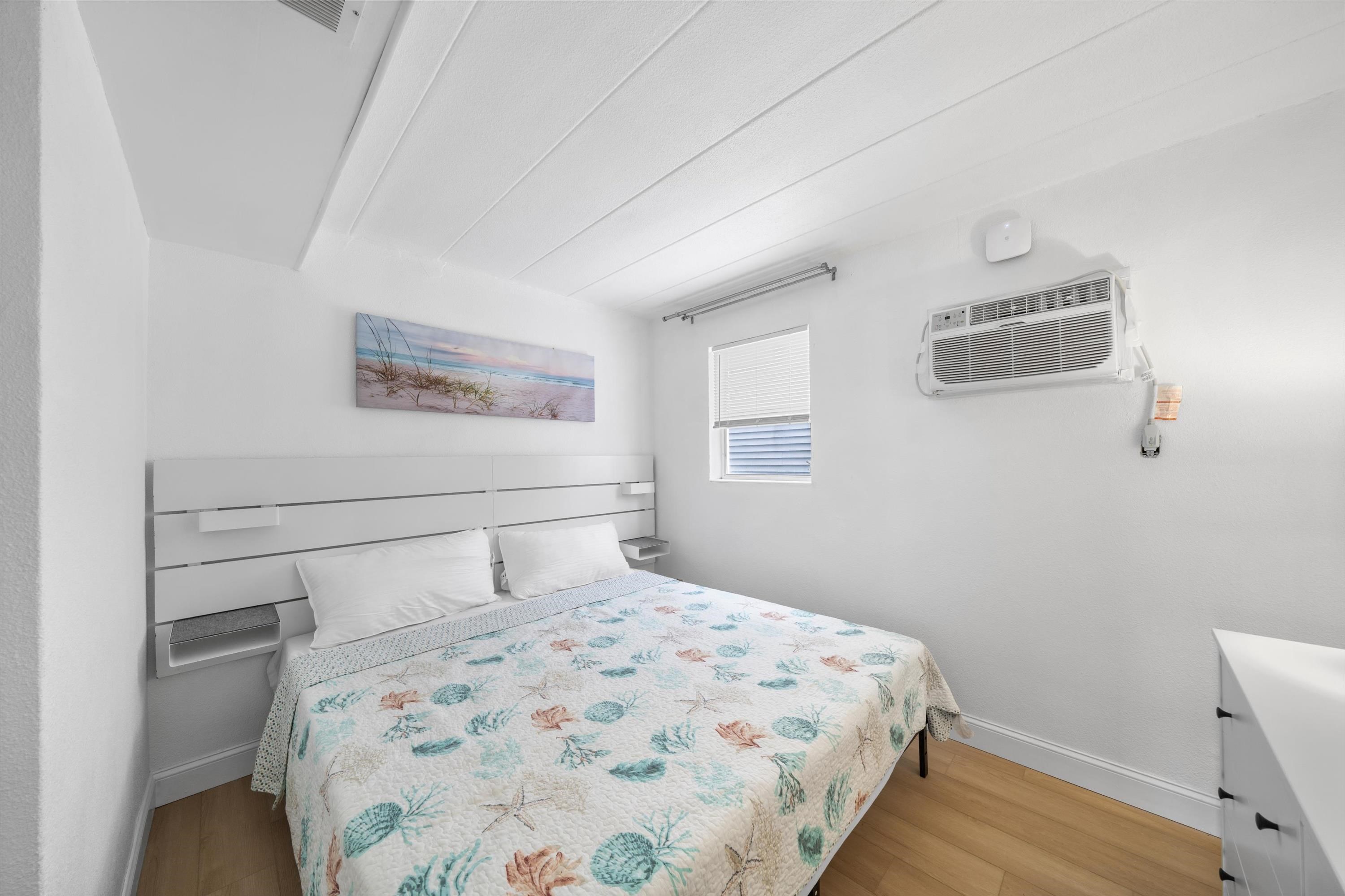 Furnished bedroom with a seashell-patterned quilt and wall-mounted air conditioner.