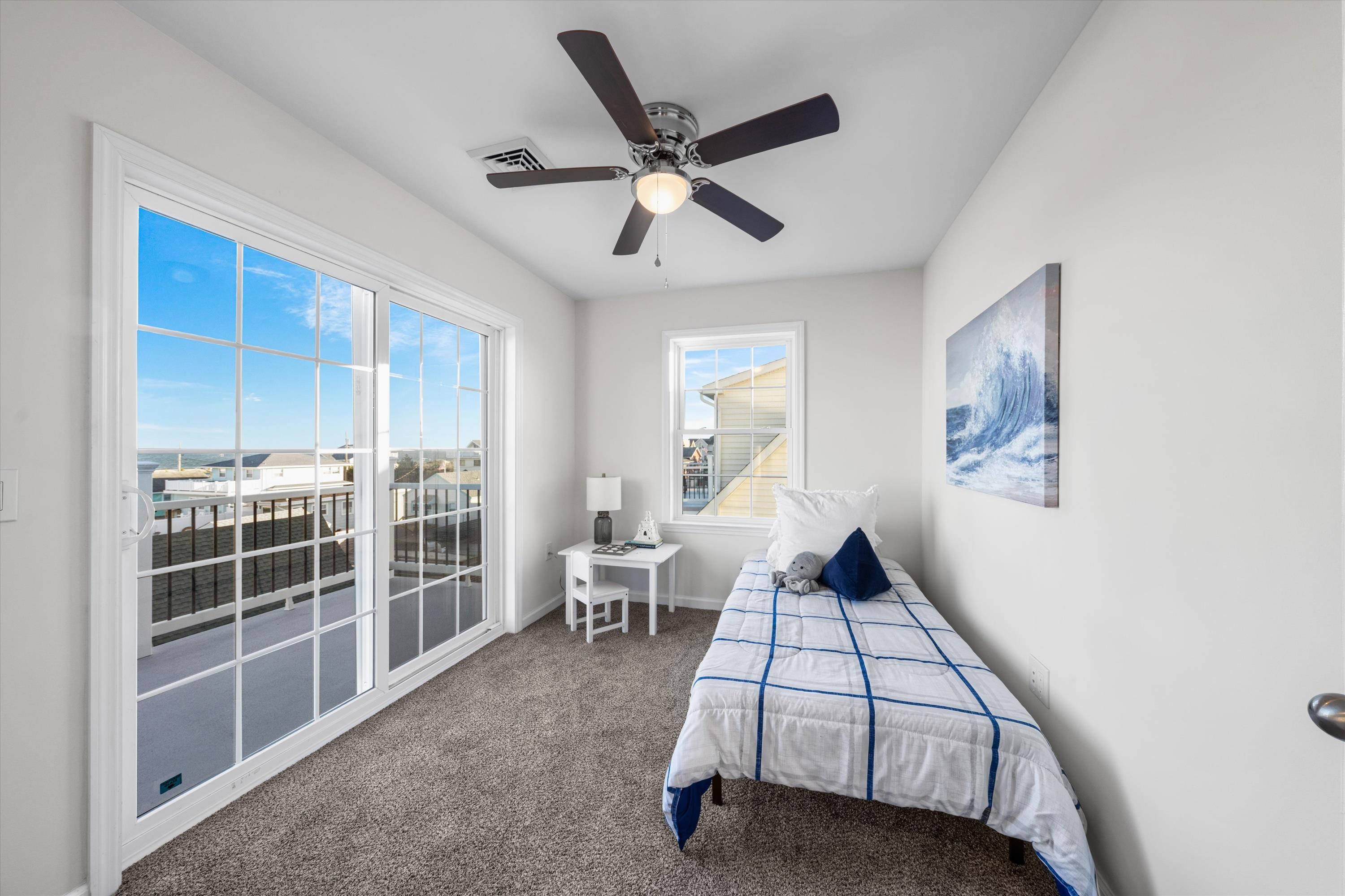 Bright bedroom with a blue-grid single bed and sliding doors overlooking the ocean.
