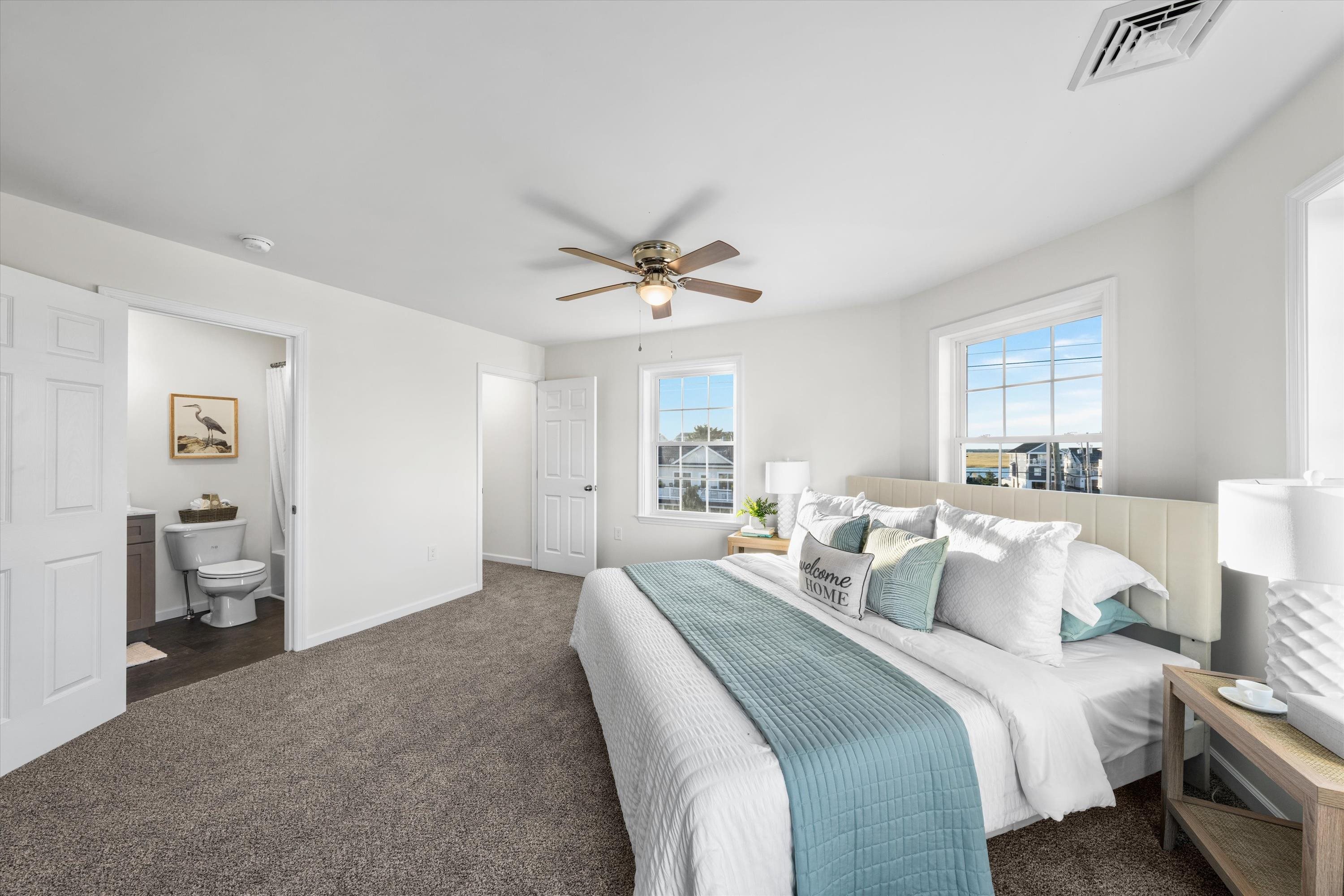 Staged bedroom with a teal bed runner, ceiling fan, and ensuite bathroom doorway.