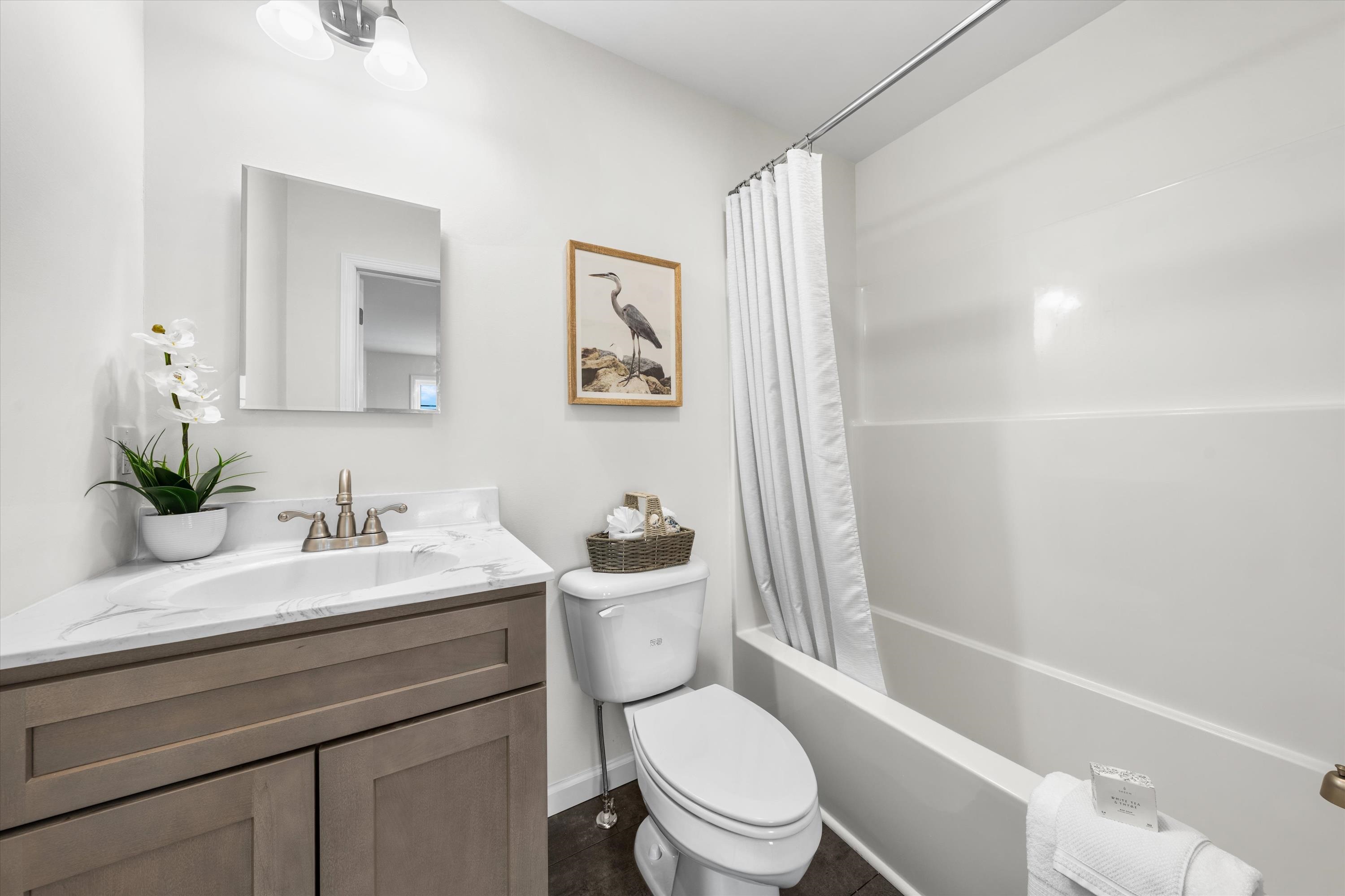Bright bathroom with a wood-tone vanity, marble-look counter, and white tub with shower curtain.