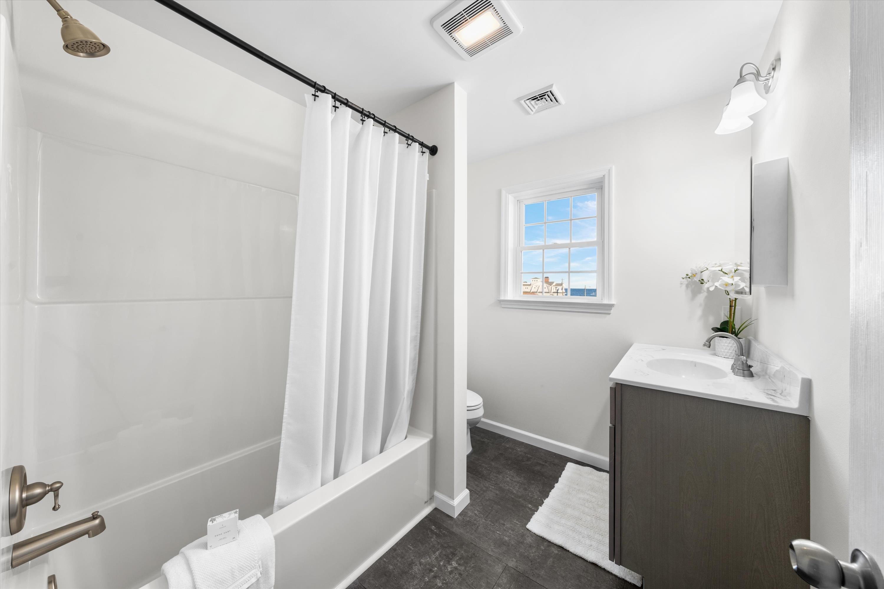 Bathroom with a curtained tub, dark vanity, and a window overlooking blue water.