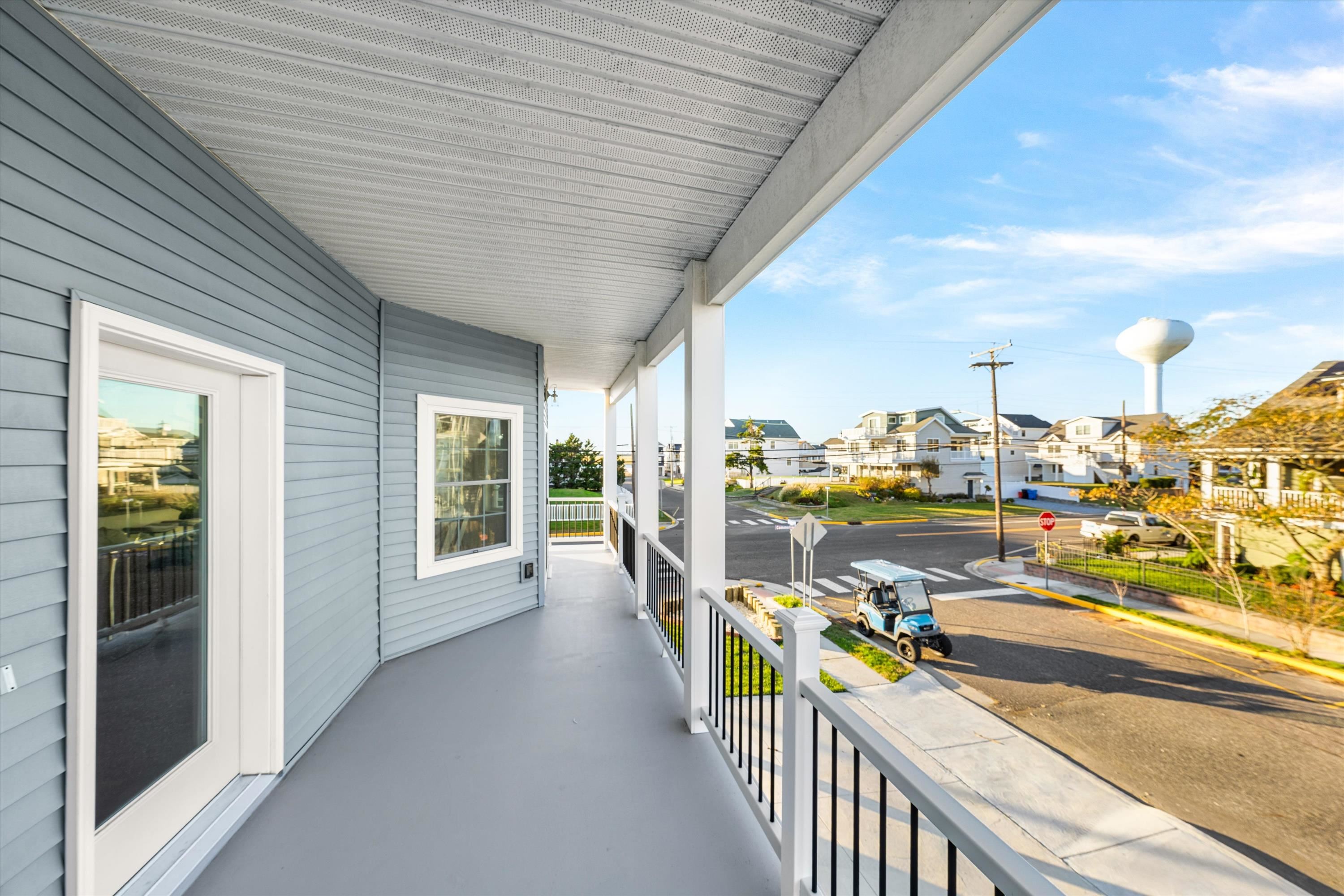 Covered porch overlooking a residential intersection, with beach-style homes and a water tower in the distance.