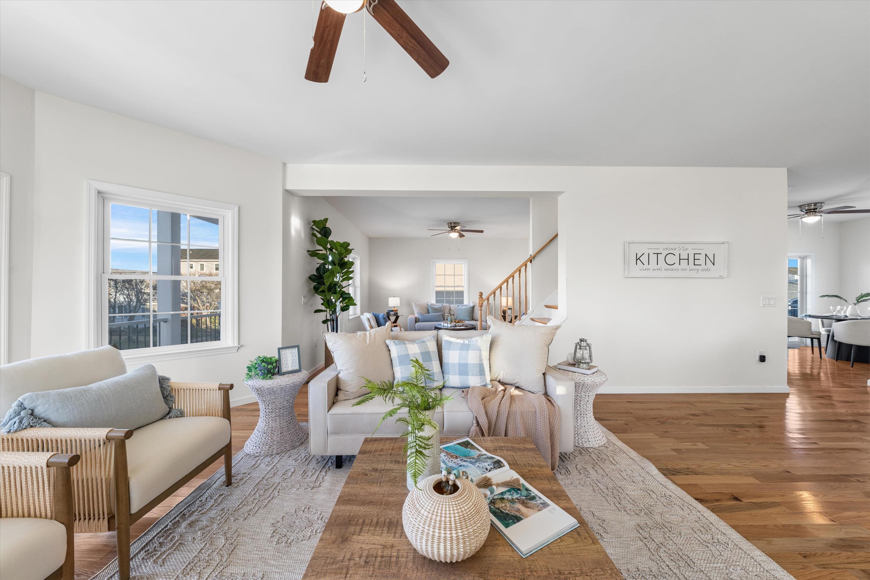 Staged living room with a pale sofa, blue-and-white cushions, hardwood floors, and an open view to the staircase.