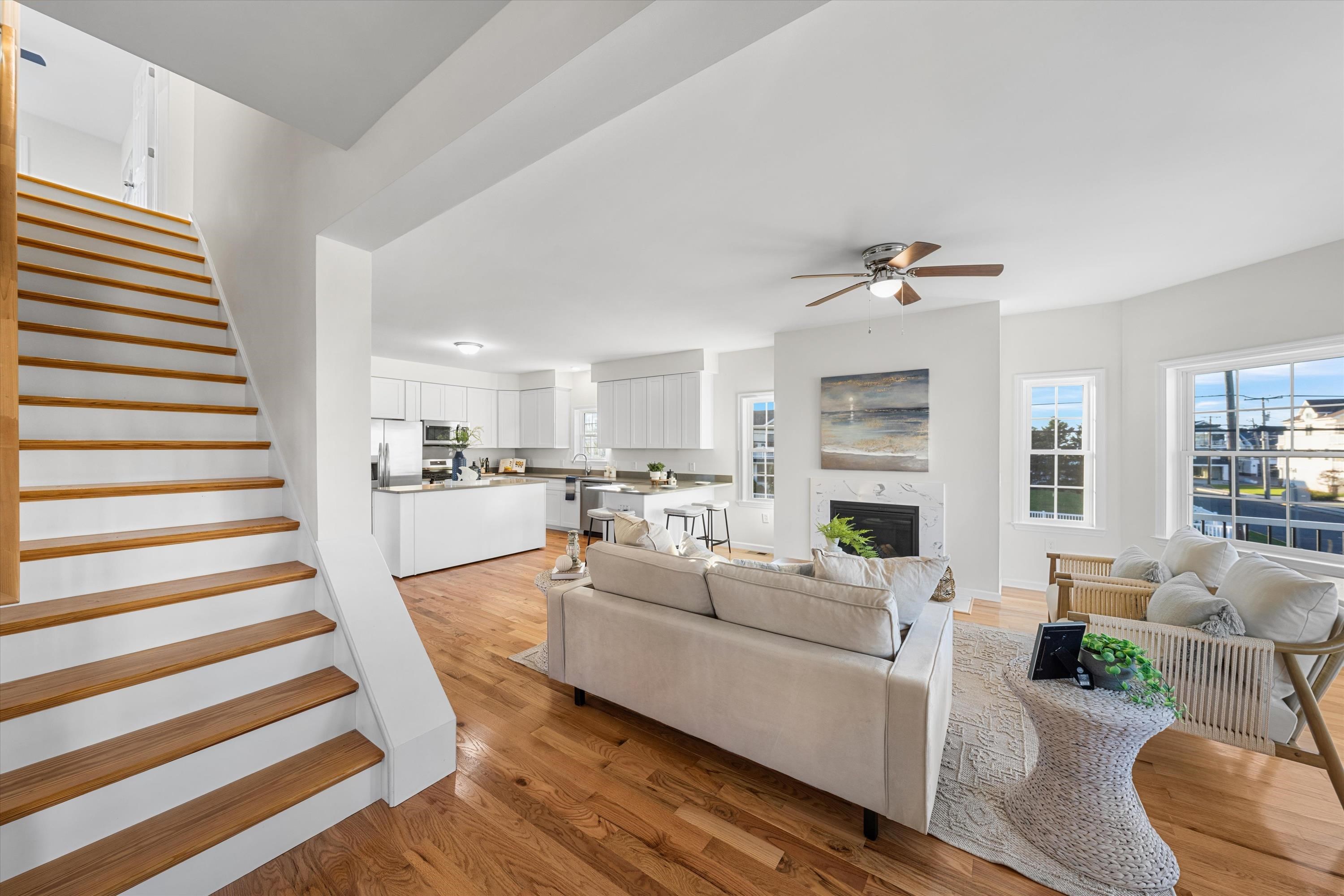 Open-plan living room and kitchen with a wood-tread staircase, fireplace, and hardwood floors.