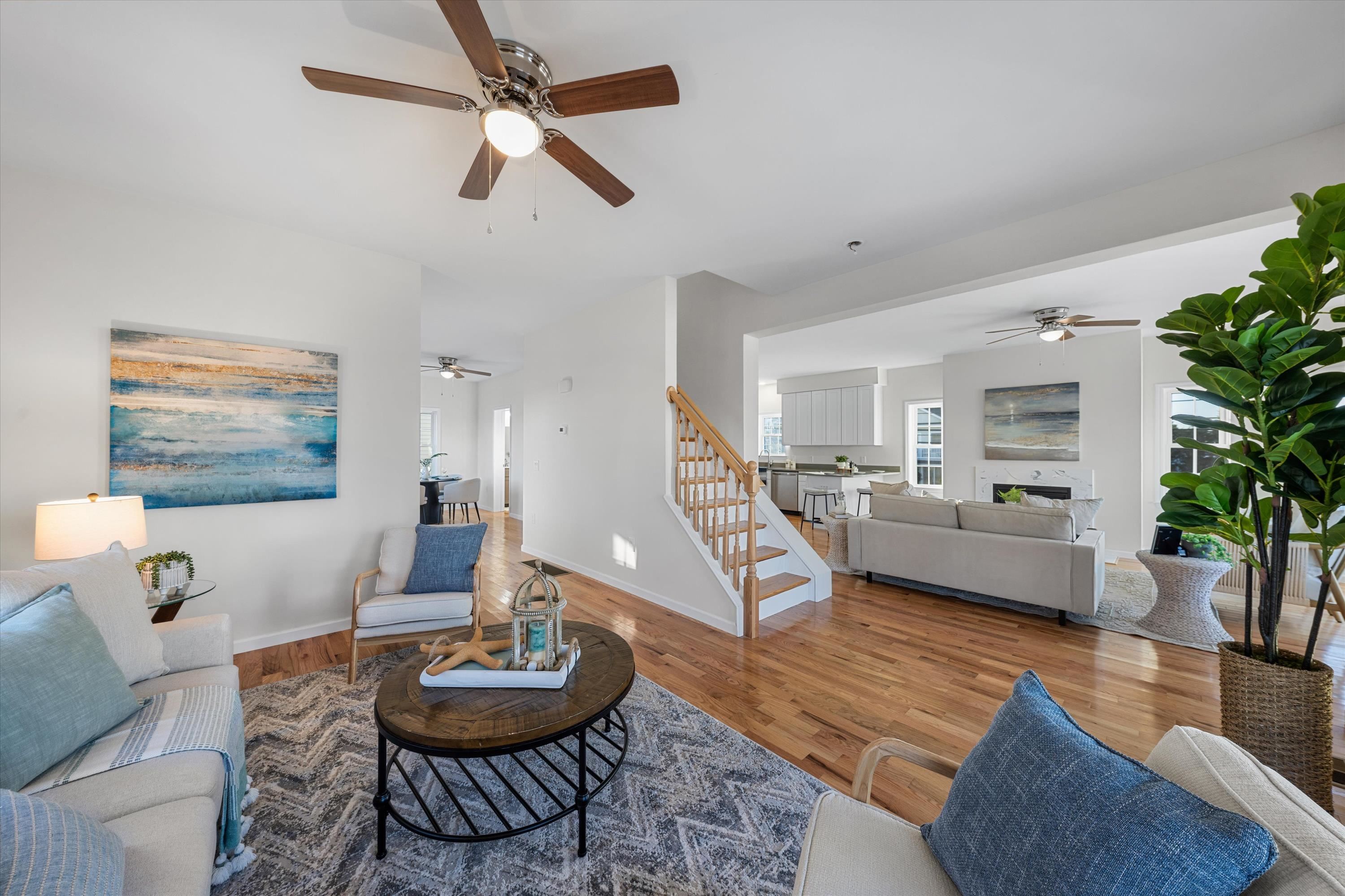 Open-plan living room with hardwood floors, a central staircase, and a bright kitchen beyond.