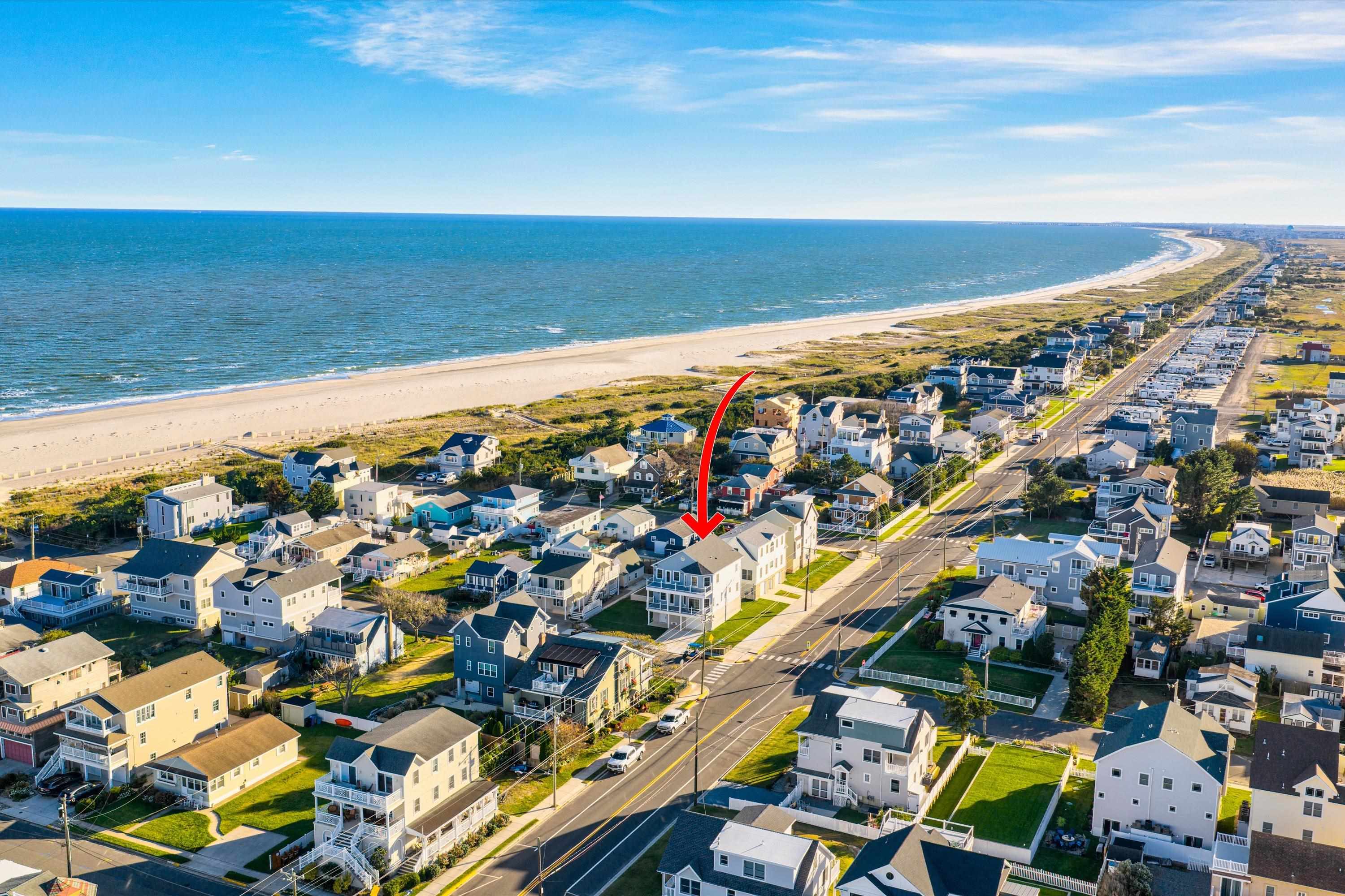 Aerial view of a coastal home marked by a red arrow, near the beach and ocean.