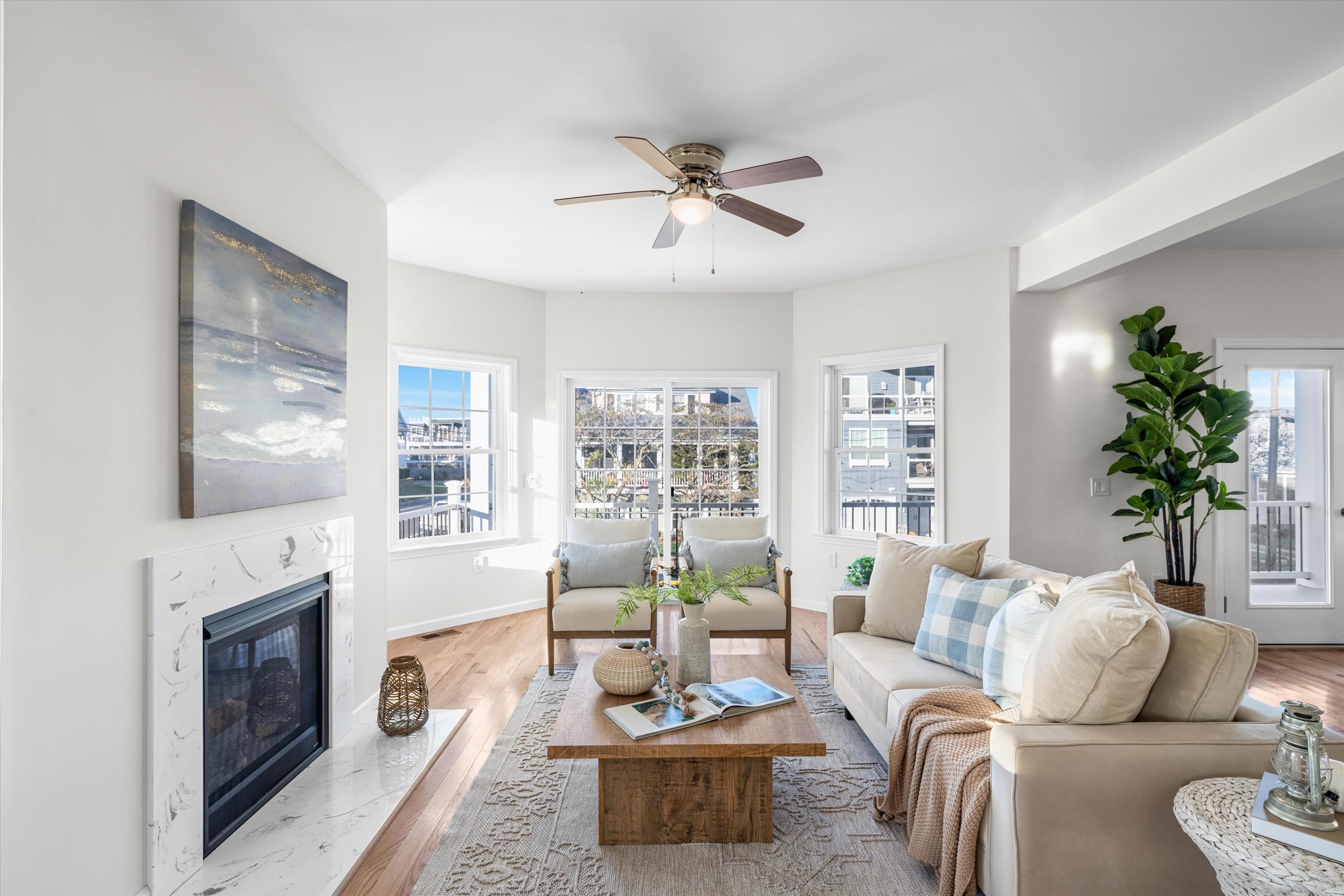 Bright living room with a marble fireplace, pale sofas, and windows overlooking neighboring homes.