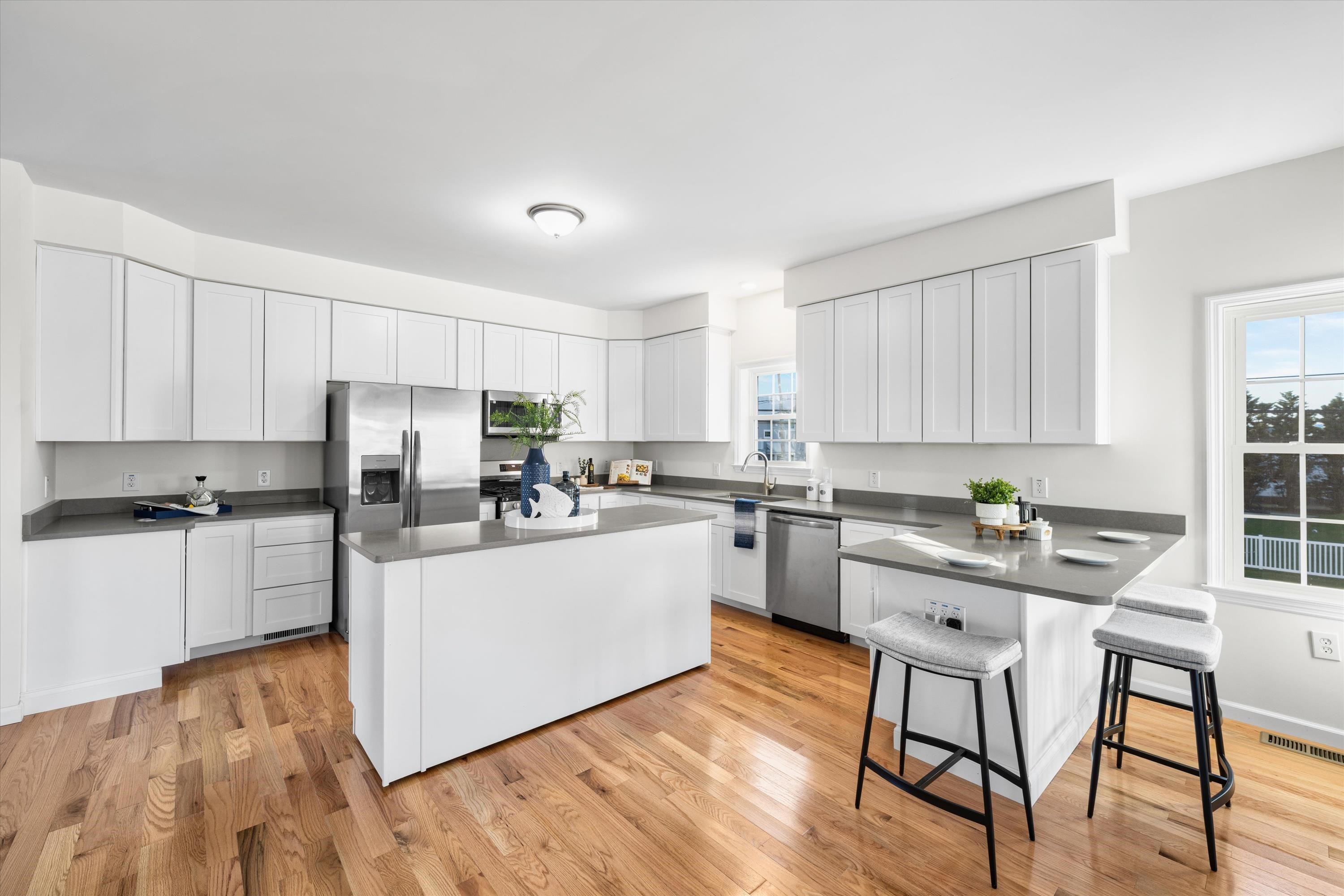 Bright kitchen with white cabinets, stainless steel appliances, a large island, and a two-stool breakfast bar.