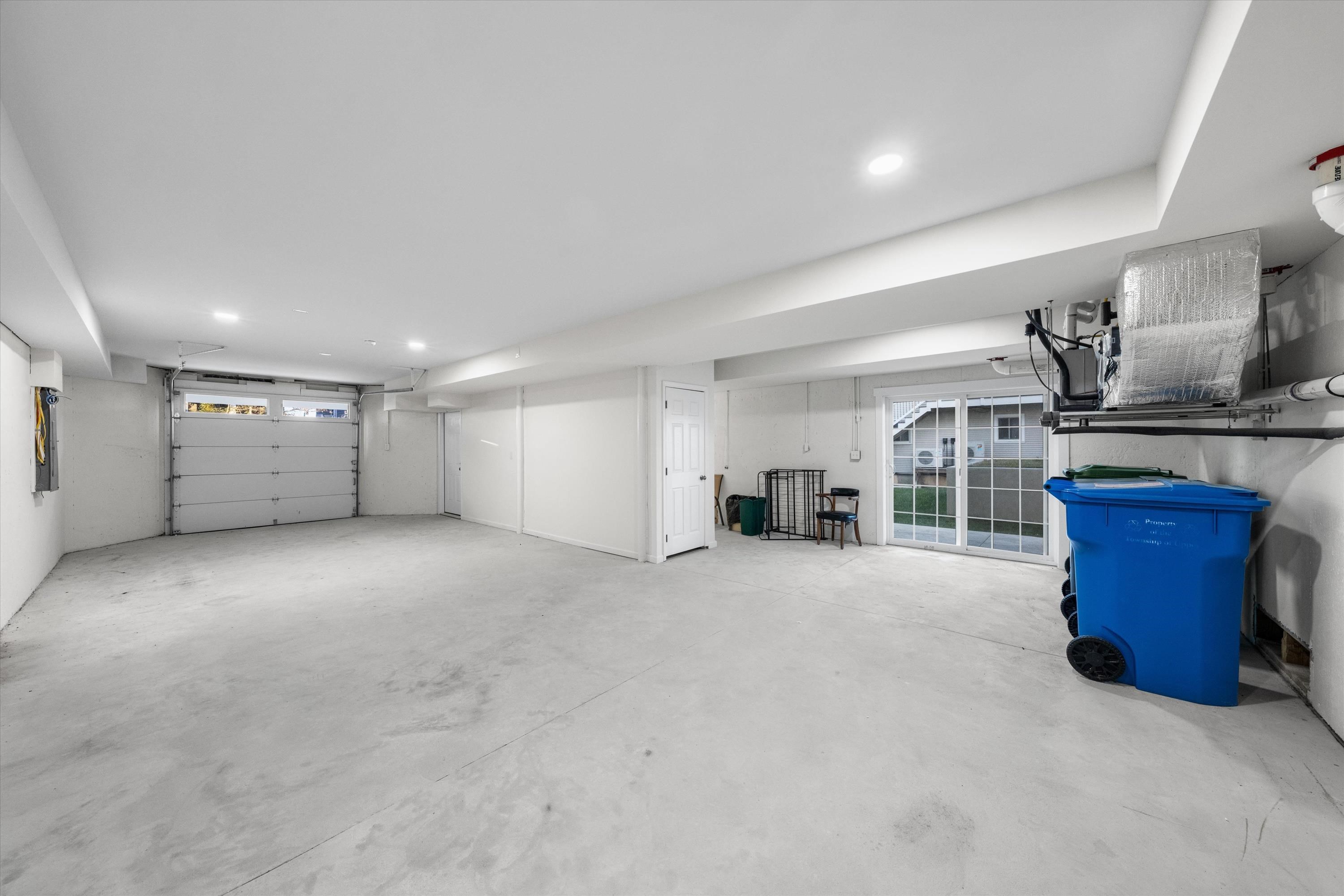 Mostly empty garage with a concrete floor, overhead door, sliding glass doors, and exposed HVAC equipment.