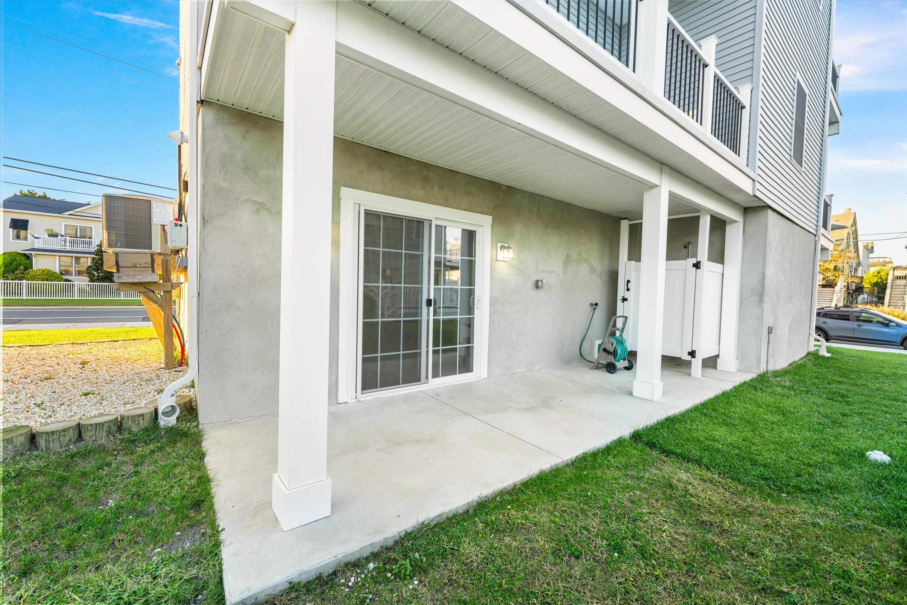 Covered concrete patio beneath a raised home, with white columns, a sliding glass door, and grassy yard.