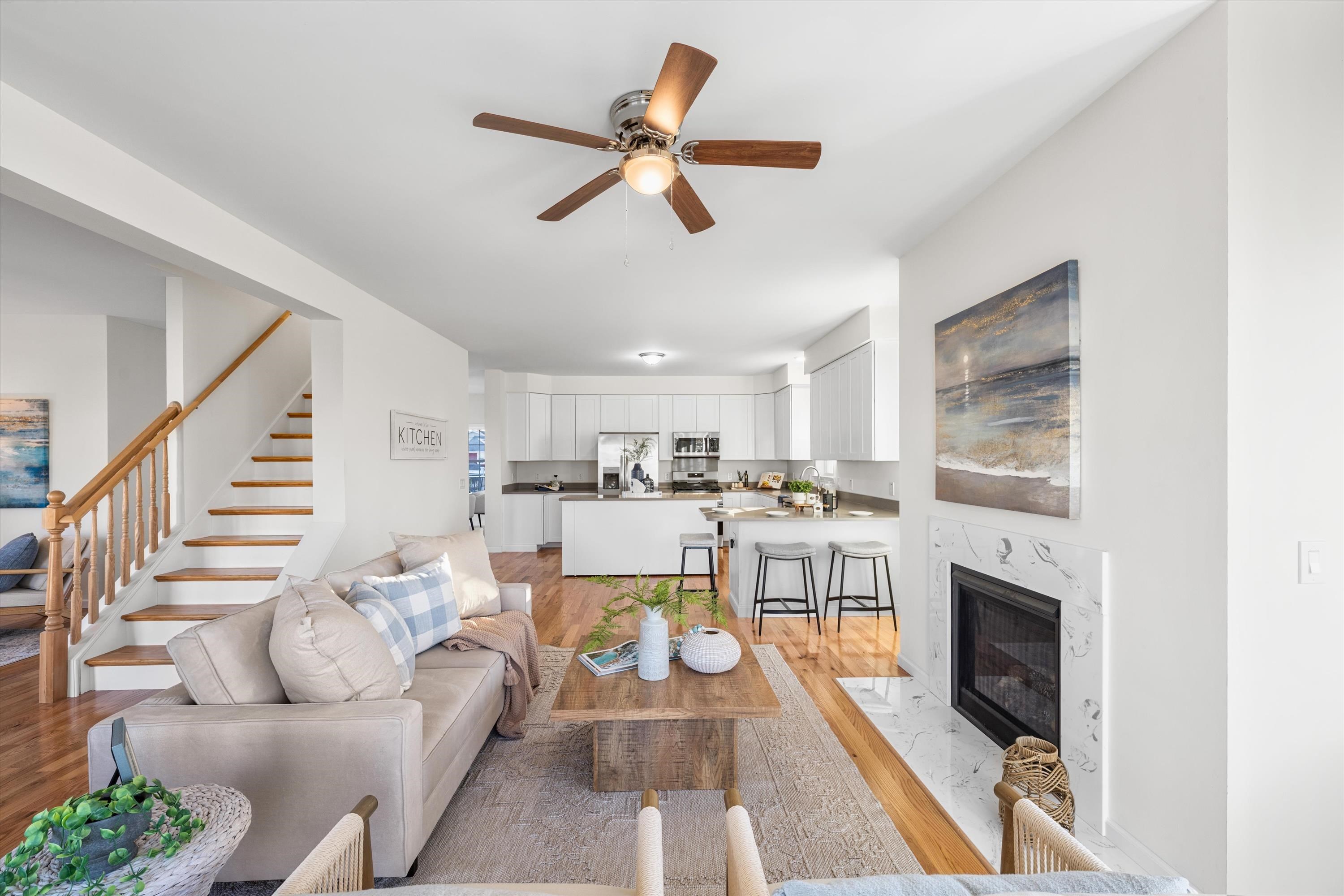 Open-plan living room and kitchen with a staircase, wood floors, and a marble-surround fireplace.