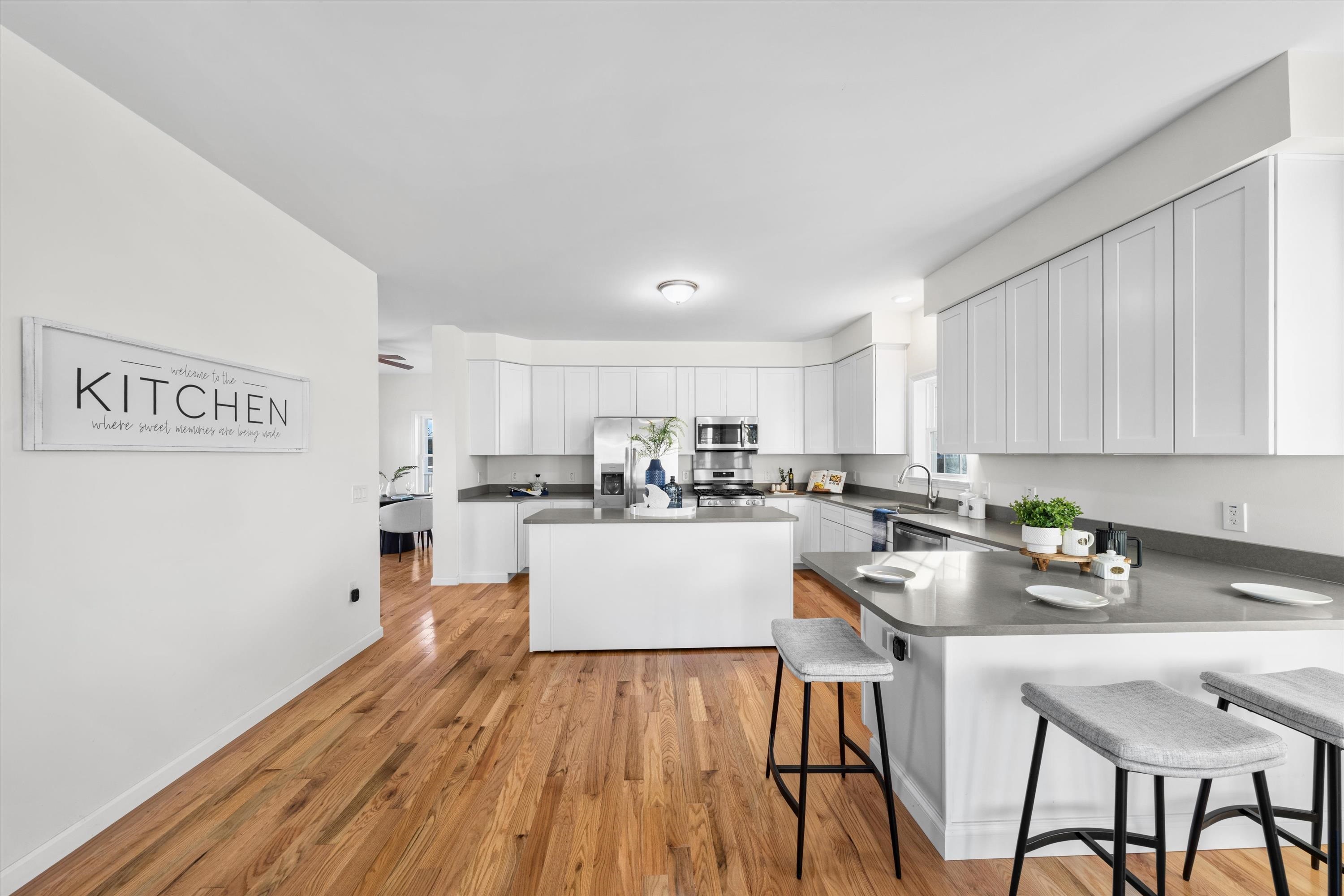 Bright kitchen with white cabinetry, stainless steel appliances, gray counters, and warm wood flooring.