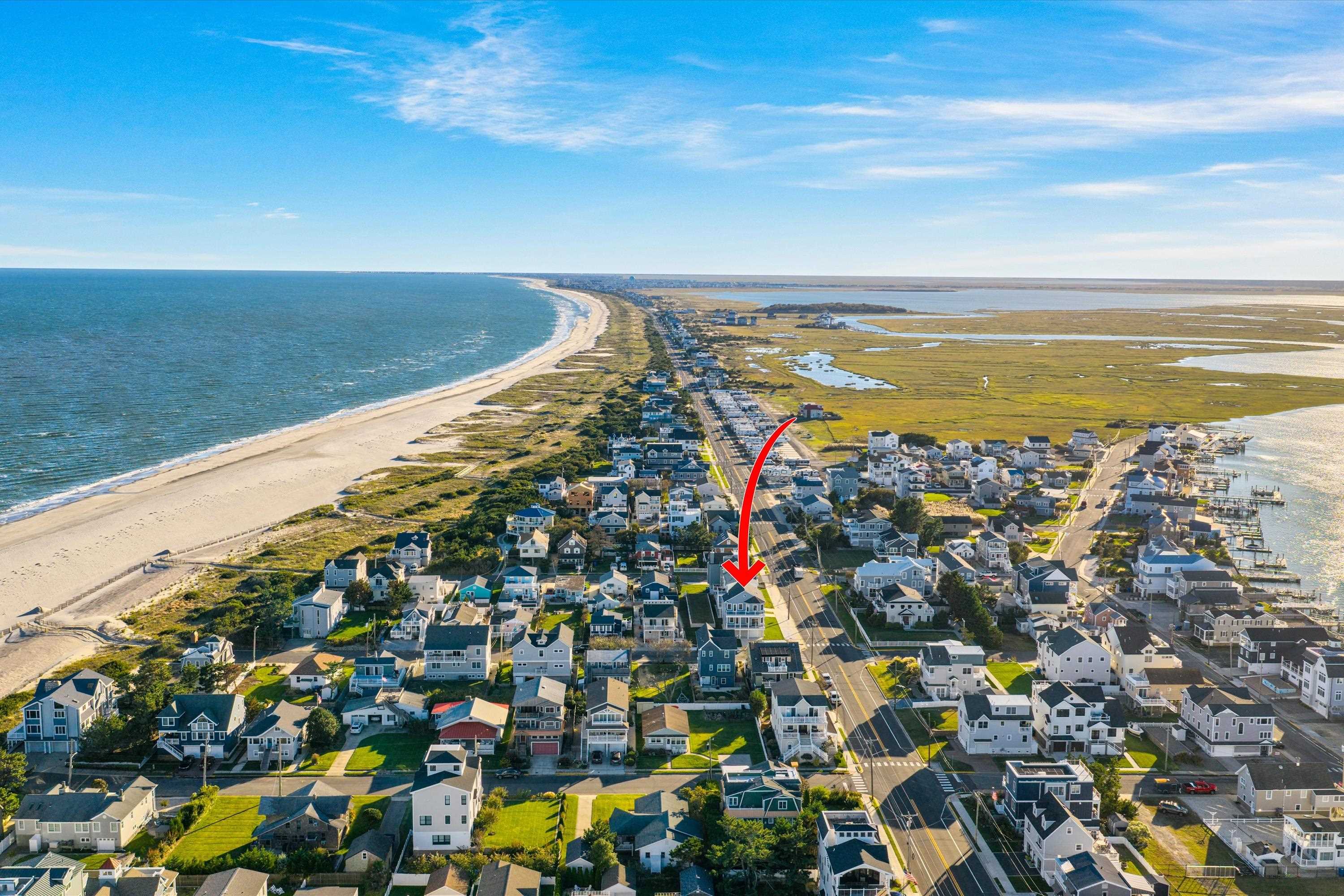 Aerial coastal neighborhood between the ocean beach and wetlands, with a red arrow marking a house.