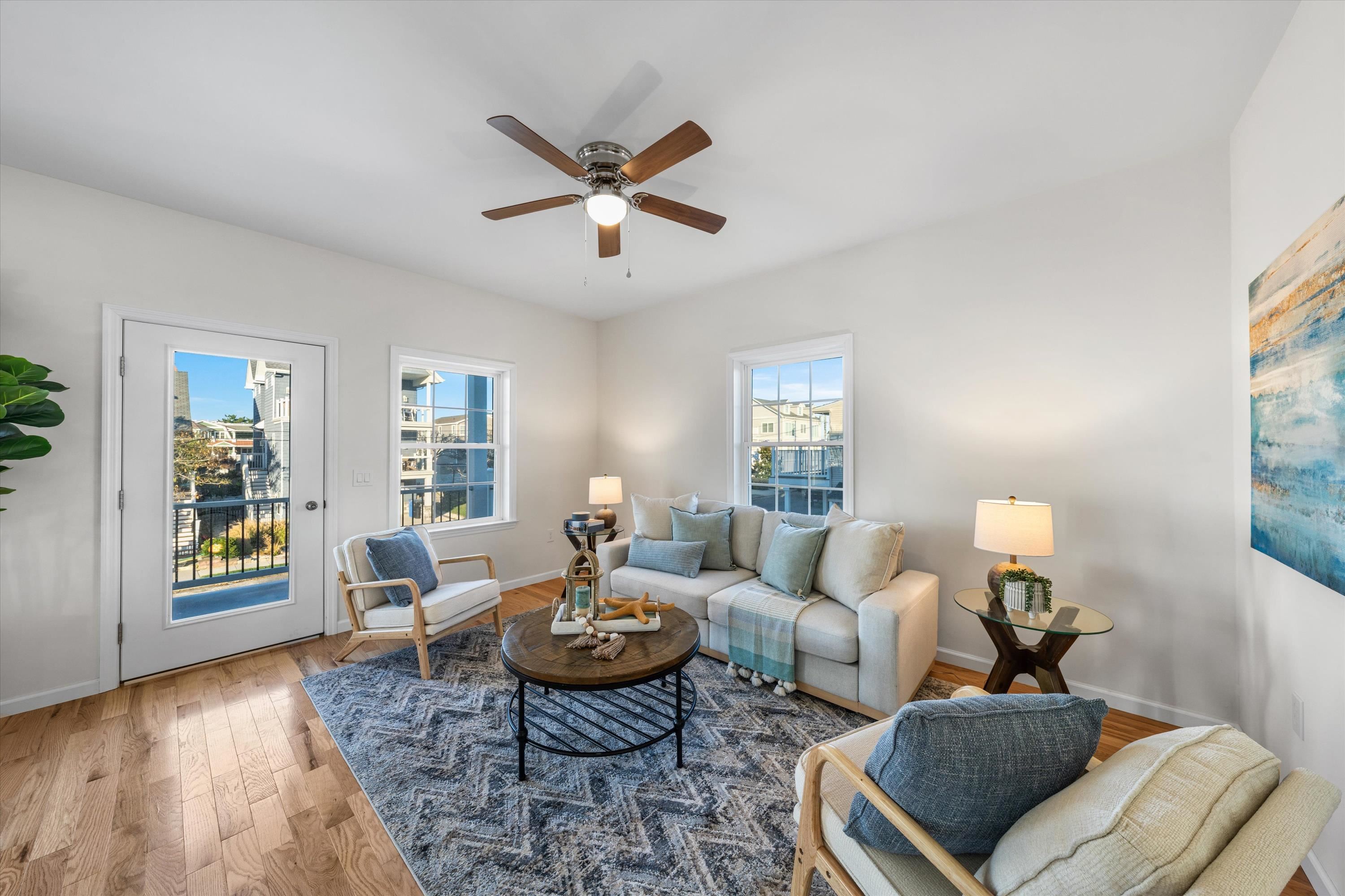 Staged living room with pale sofas, wood floors, and windows overlooking neighboring homes.