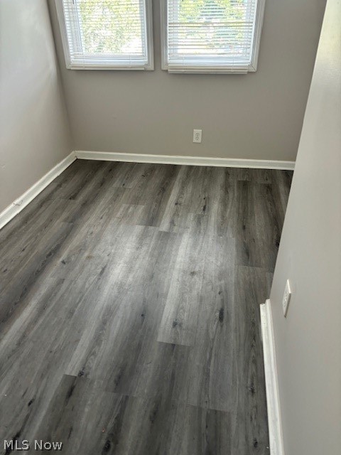 Empty room with gray wood-look flooring and two windows with blinds.
