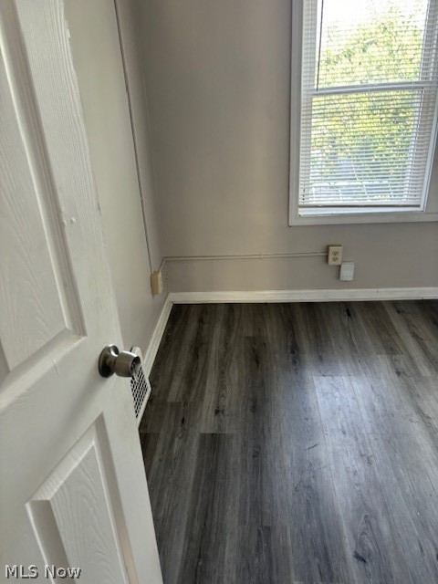 Vacant room with dark wood-look flooring, a window with blinds, and an open white door.