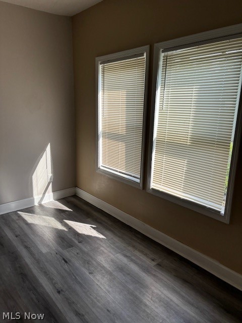 Empty room with gray flooring, two windows with blinds, and sunlight across the floor.