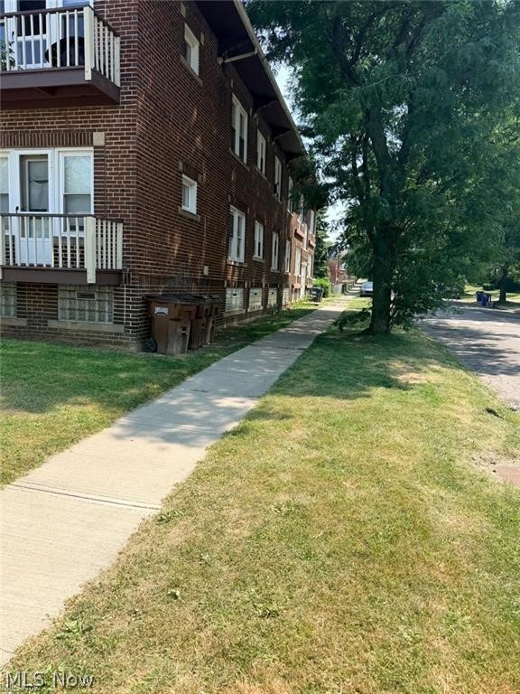 Brick apartment building with balconies beside a sidewalk and mature tree.
