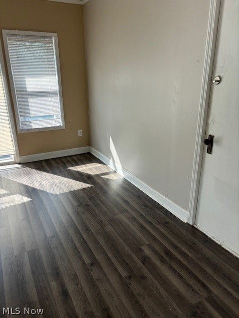 Empty room with dark plank flooring, a window with blinds, and sunlight across the floor.