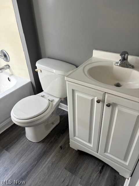 Bathroom with a white tub, toilet, and paneled vanity on gray plank flooring.