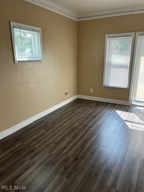 Empty room with tan walls, dark wood-look flooring, and windows with blinds.