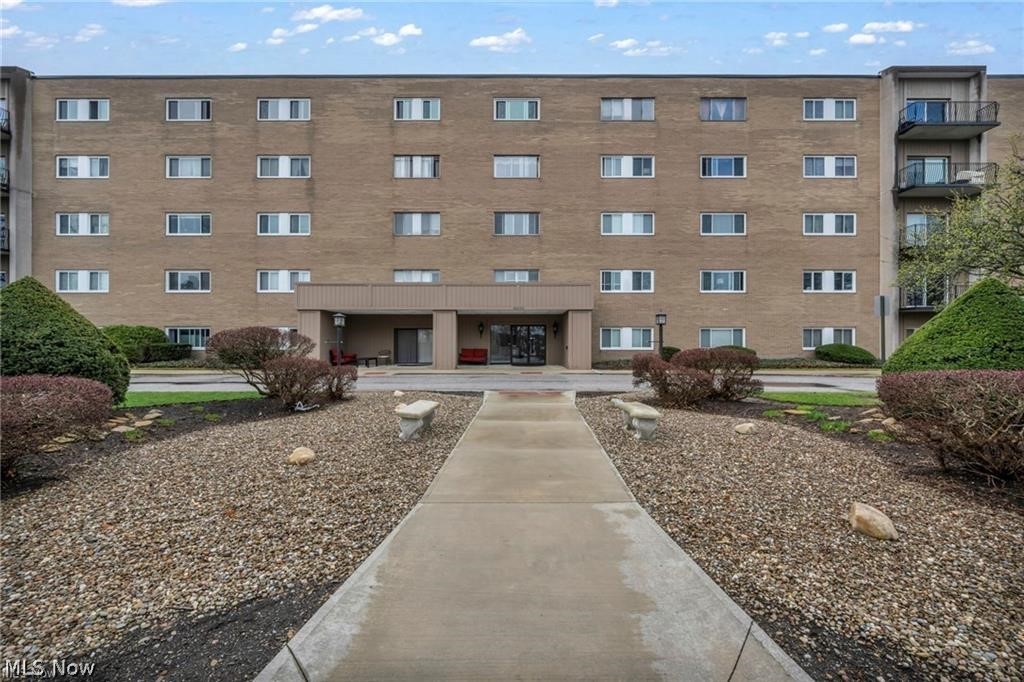 Brick condominium building with a covered entrance, balconies, and a walkway through landscaped grounds.