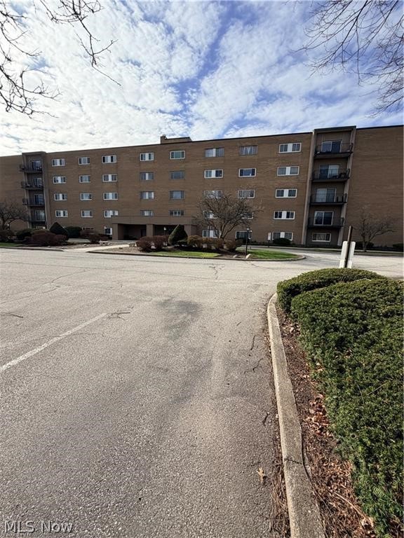 Brown brick apartment building with rows of windows and balconies across a paved drive.