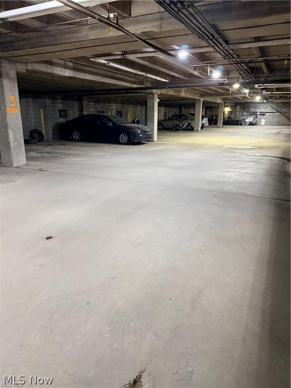 Underground parking garage with concrete support columns, overhead pipes, and parked cars.