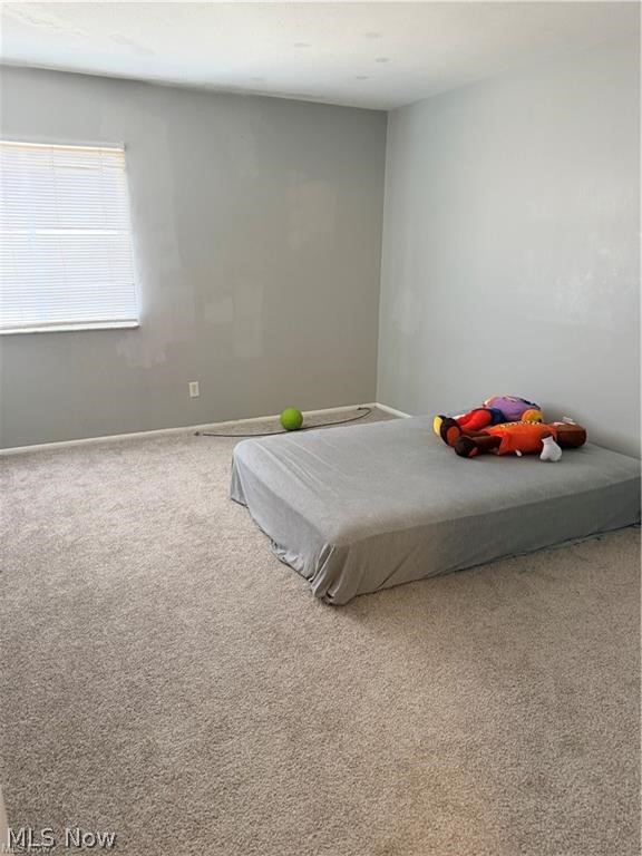 Bedroom with gray walls, beige carpet, a window with blinds, and a mattress with colorful toys.