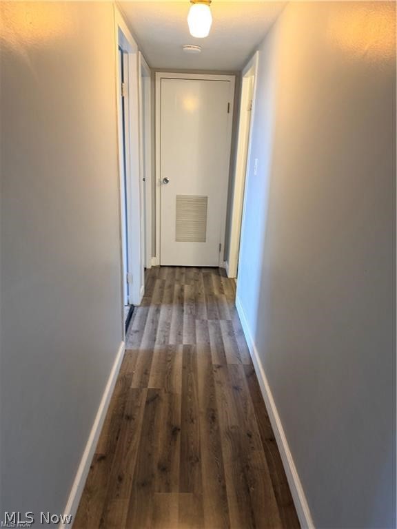 Narrow hallway with wood-look flooring leading to a white door with a vent.