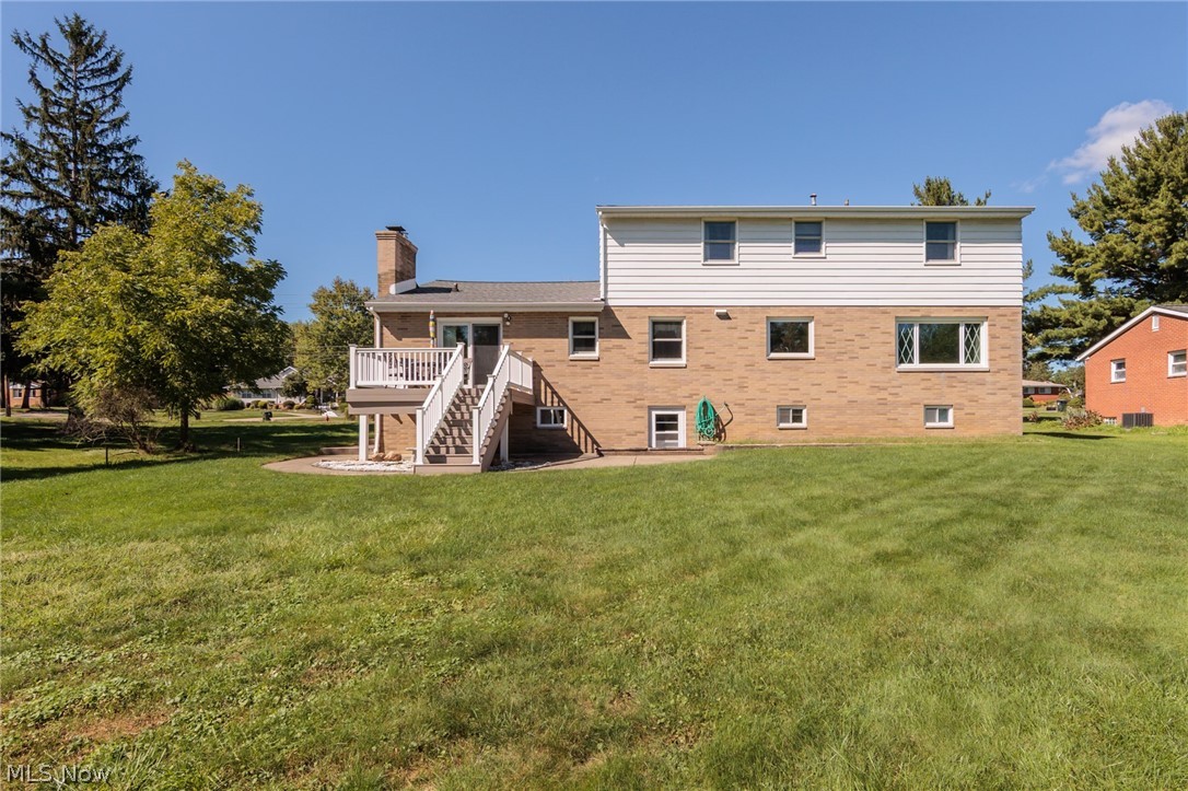 Rear of a brick-and-siding house with an elevated deck, exterior stairs, and a broad lawn.
