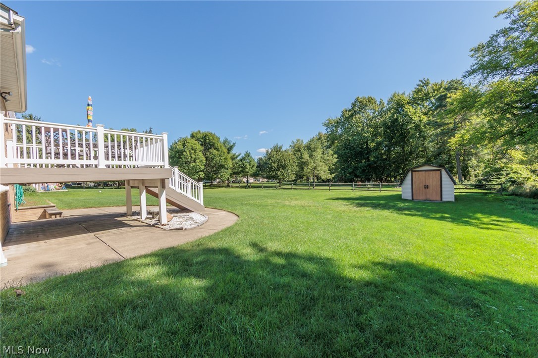 Backyard with a raised deck, broad lawn, fenced tree line, and storage shed.