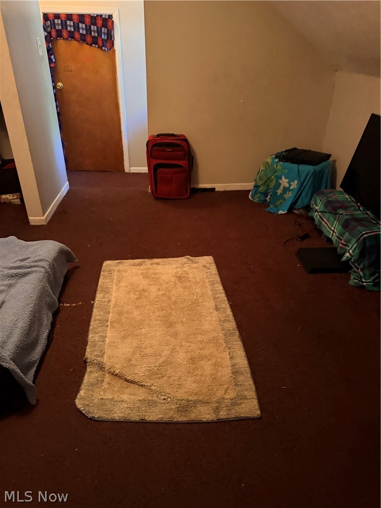 Bedroom with dark carpet, a tan rug, red suitcase, and plaid curtain over the door.