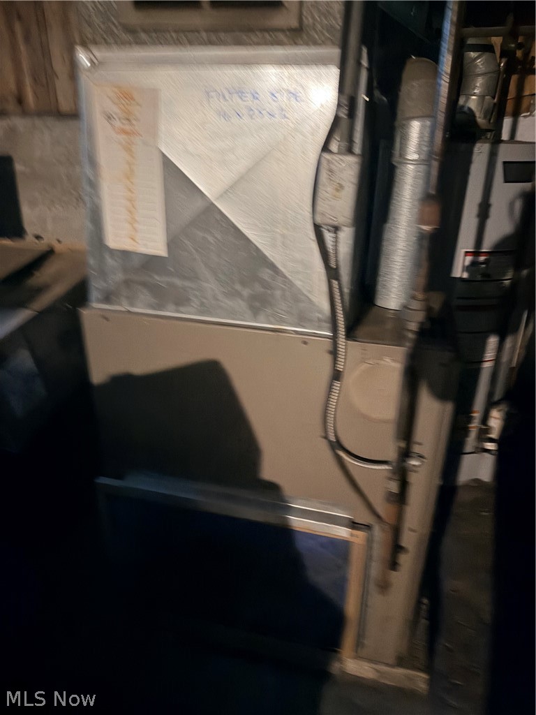 Basement HVAC equipment with a large metal duct and connected pipes.