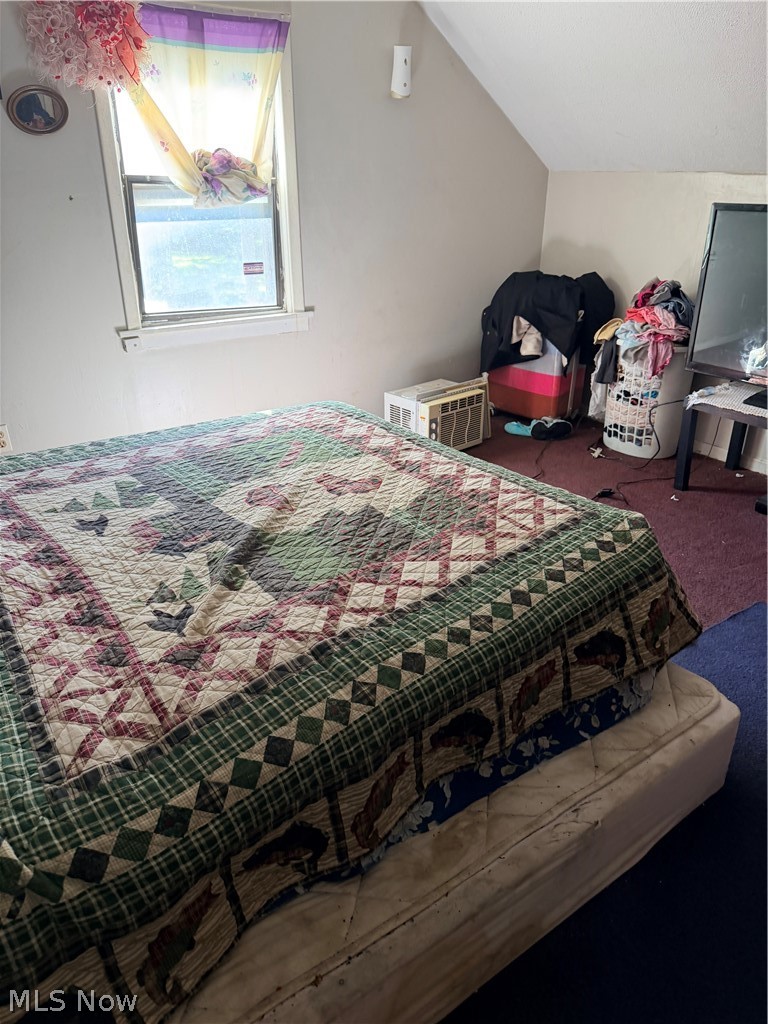 Bedroom with a patterned quilt-covered bed, colorful window curtains, and a sloped ceiling.