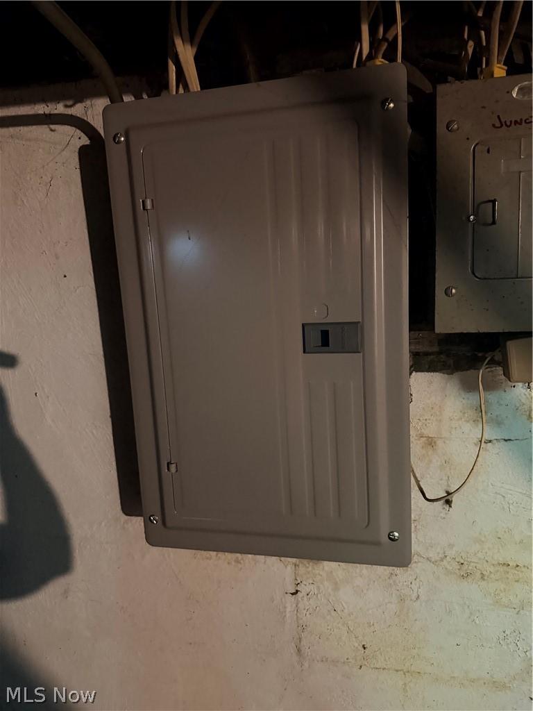 Basement electrical panel beside an older panel, with exposed wiring overhead.