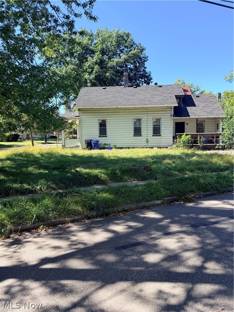 Rear of a light-colored house with a covered porch and overgrown grassy yard.