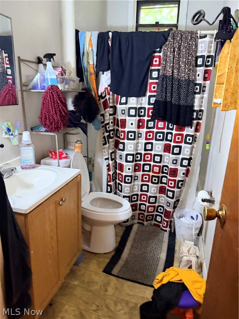 Bathroom with a patterned shower curtain, wood vanity, toilet, and clothes hanging to dry.