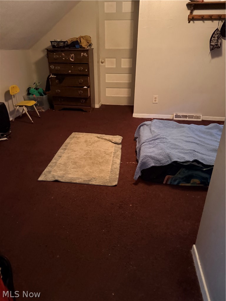 Bedroom with brown carpet, a wooden dresser, and a low bed beneath a sloped ceiling.