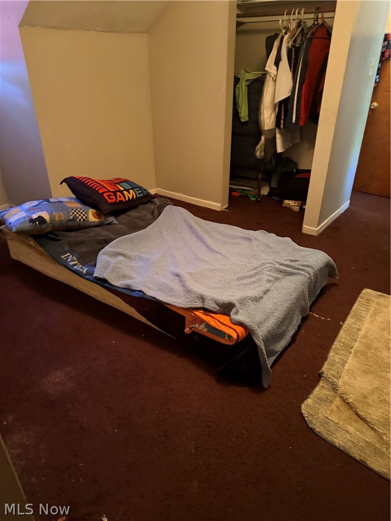 Bedroom with a low bed, gray blanket, sports-themed pillows, and an open clothes closet.
